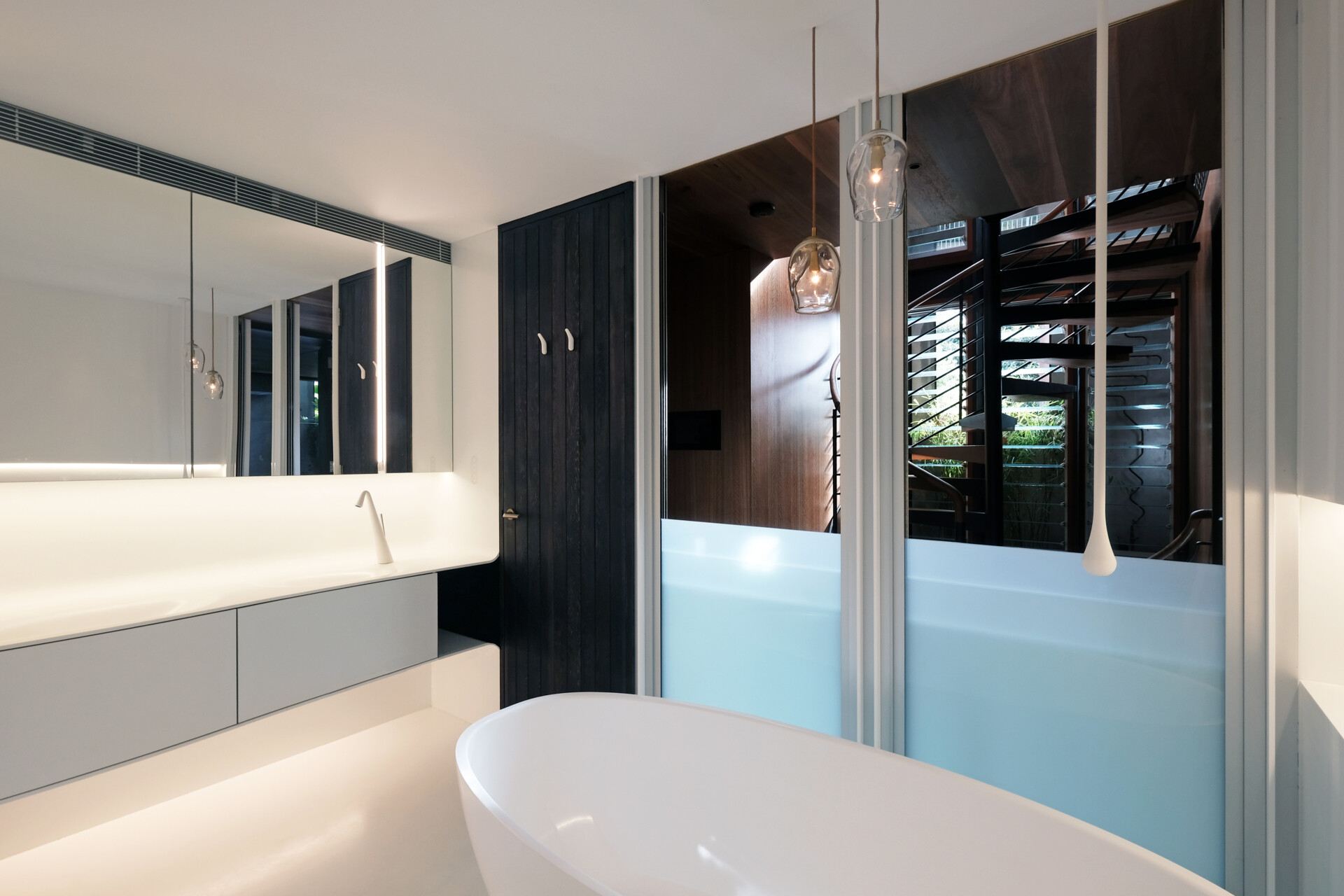 Crisp white finishes and seamless cabinetry give this bathroom a pared-back, contemporary feel. A floating double vanity and sculptural tapware reinforce the clean lines, while concealed lighting adds a soft, ambient glow. A timber door introduces warmth, offering a quiet contrast to the otherwise minimal palette.