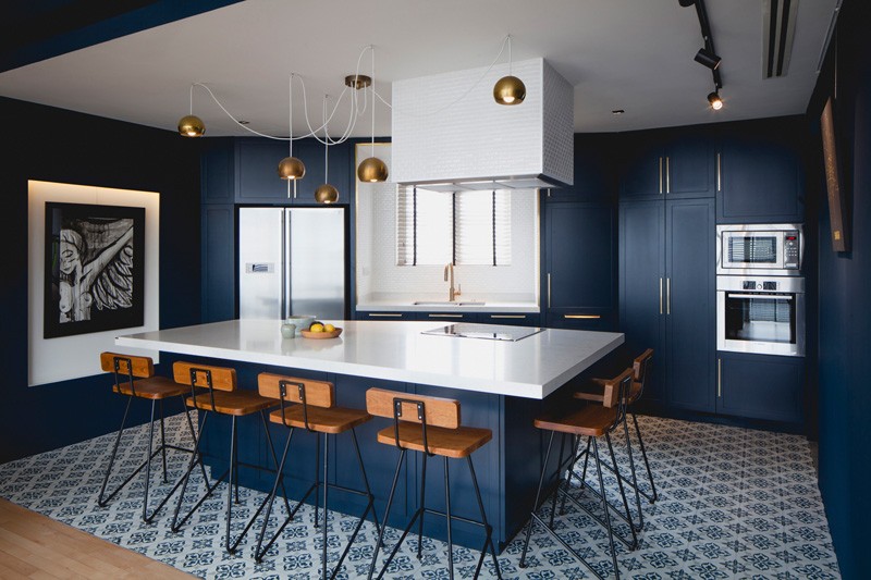 Cobalt blue walls and cabinets unify the kitchen and dining zone, with brass accents and patterned tile adding character.