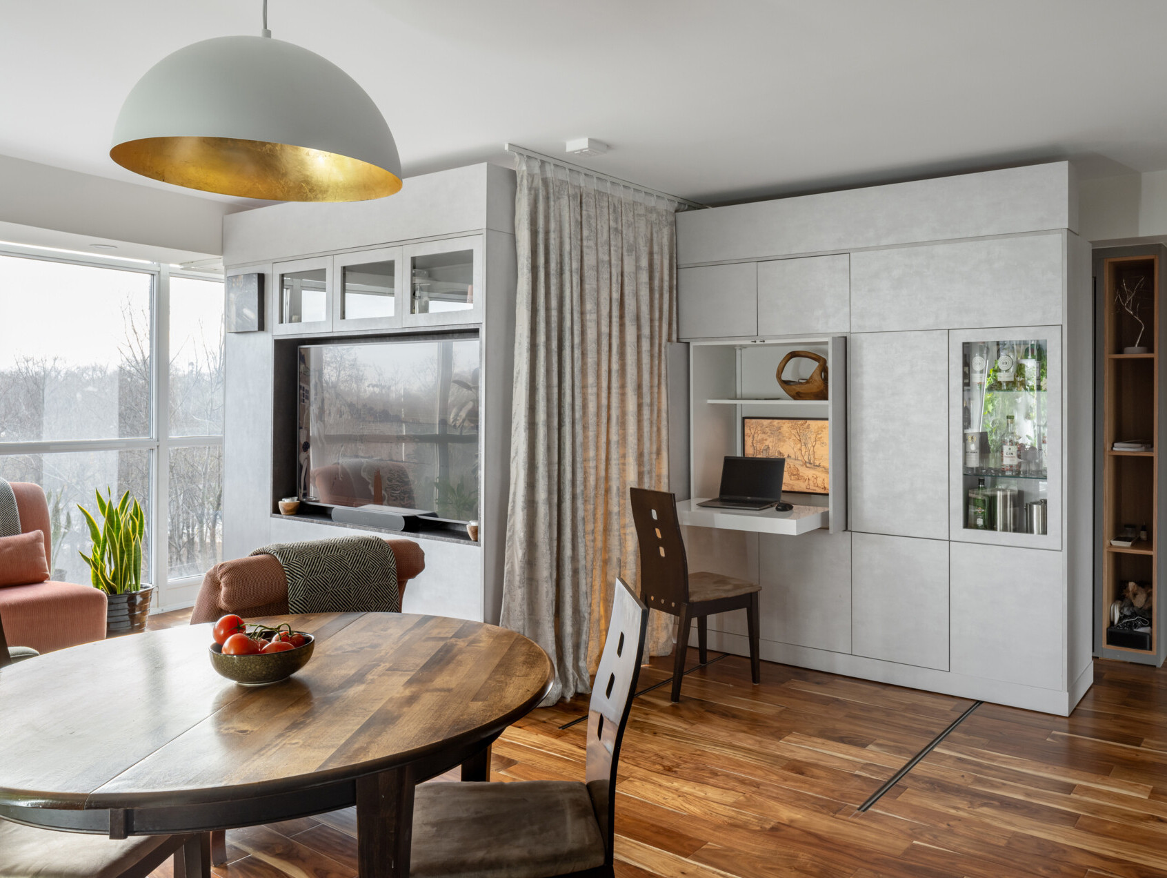 A modern apartment has clever movable walls, packed with storage, a desk, and entertainment features. Behind the walls is a space that gets transformed into a bedroom.