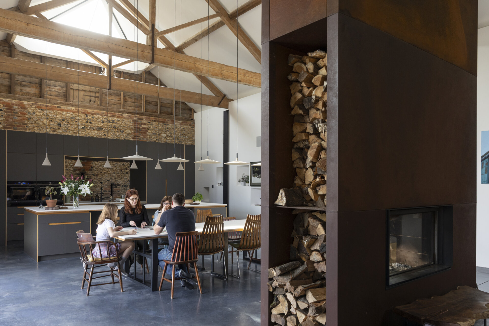 Polished concrete floors and industrial fittings provide a crisp backdrop for this dining area and kitchen that are softened by warm wood accents and custom furnishings.