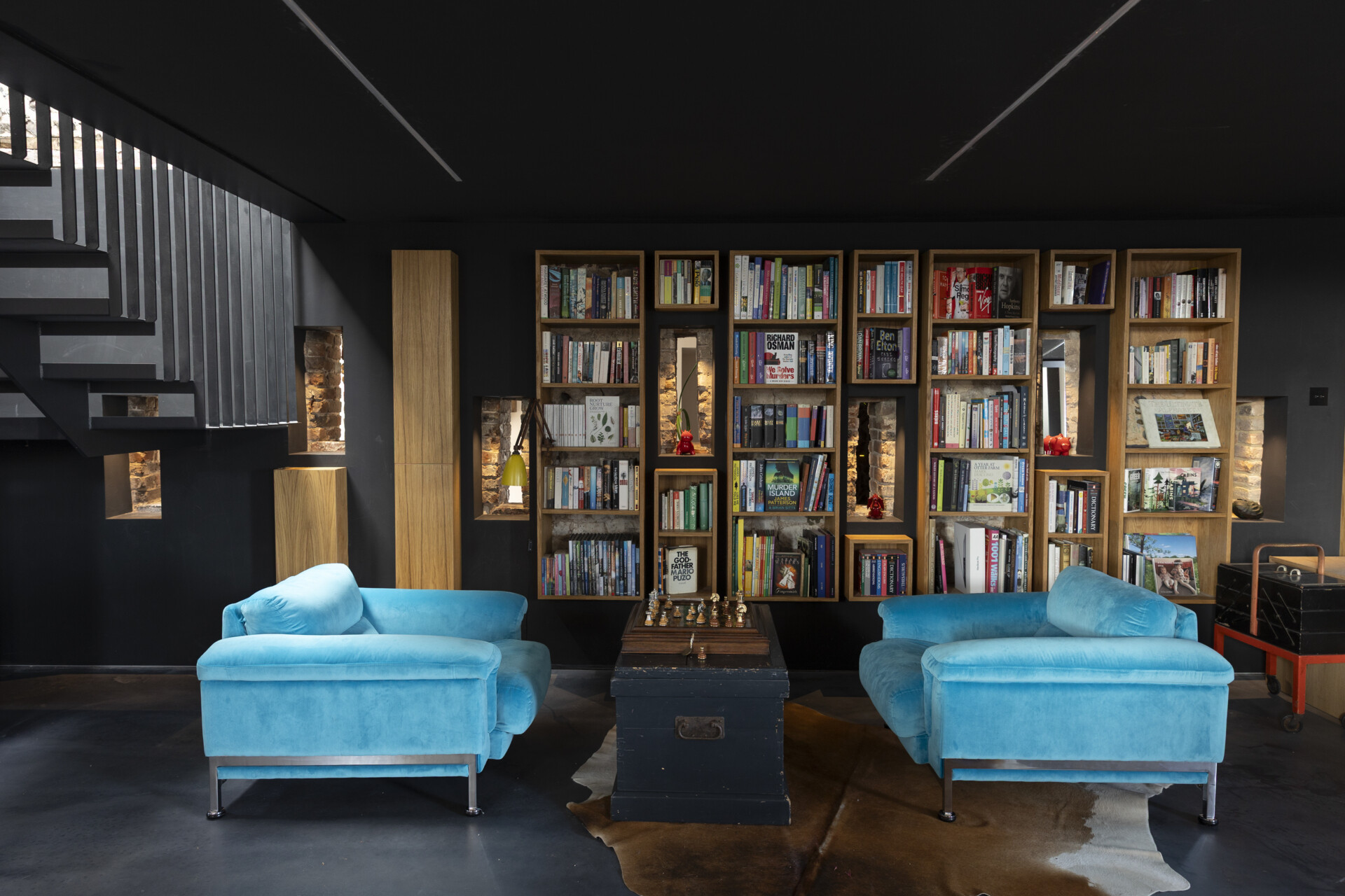 The bespoke steel staircase doubles as a sculptural centerpiece and a functional link between levels. Nearby, the library tucks into a quieter corner of the home, framed by matte black walls and flooded with soft natural light from small windows.