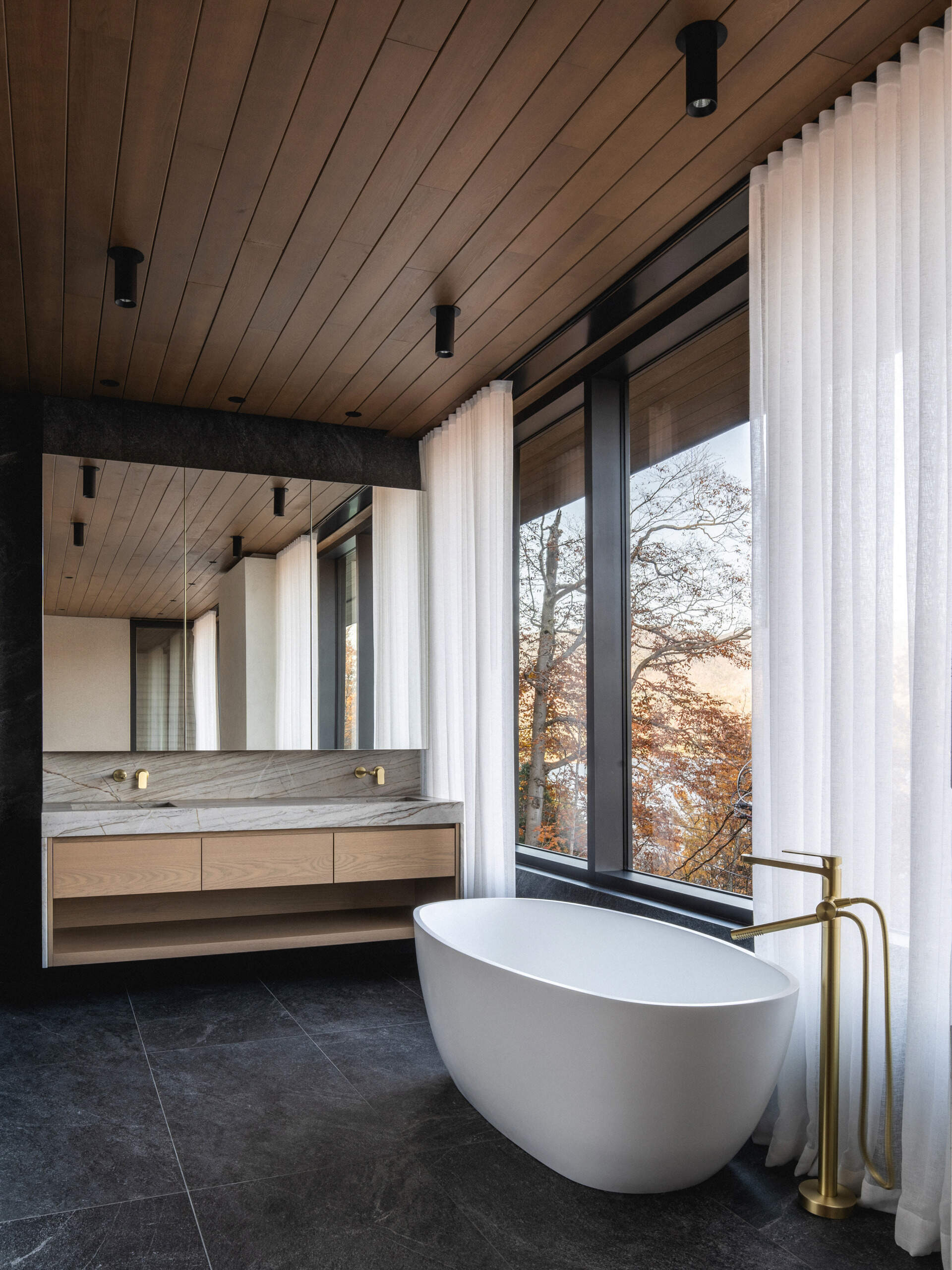An ensuite bathroom features a stone-clad shower and a freestanding tub positioned to face the scenery.