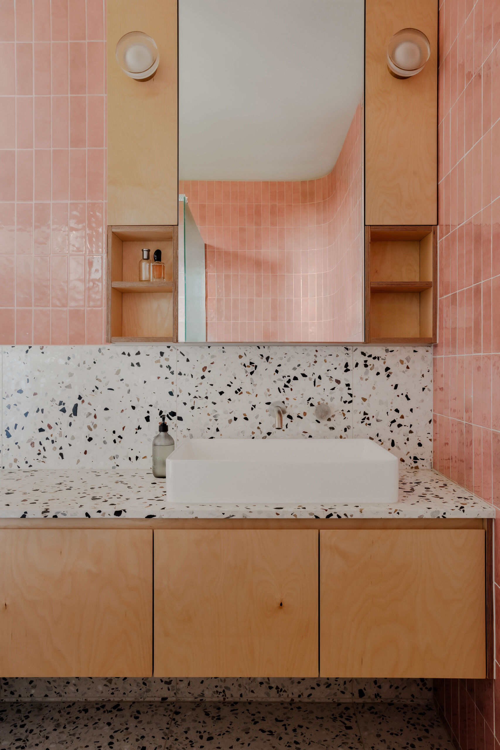 This bathroom pairs soft pink glazed tiles with a terrazzo vanity for a playful yet calming feel. Floating timber cabinetry and built-in shelving add warmth and function, creating a space that’s both practical and inviting.
