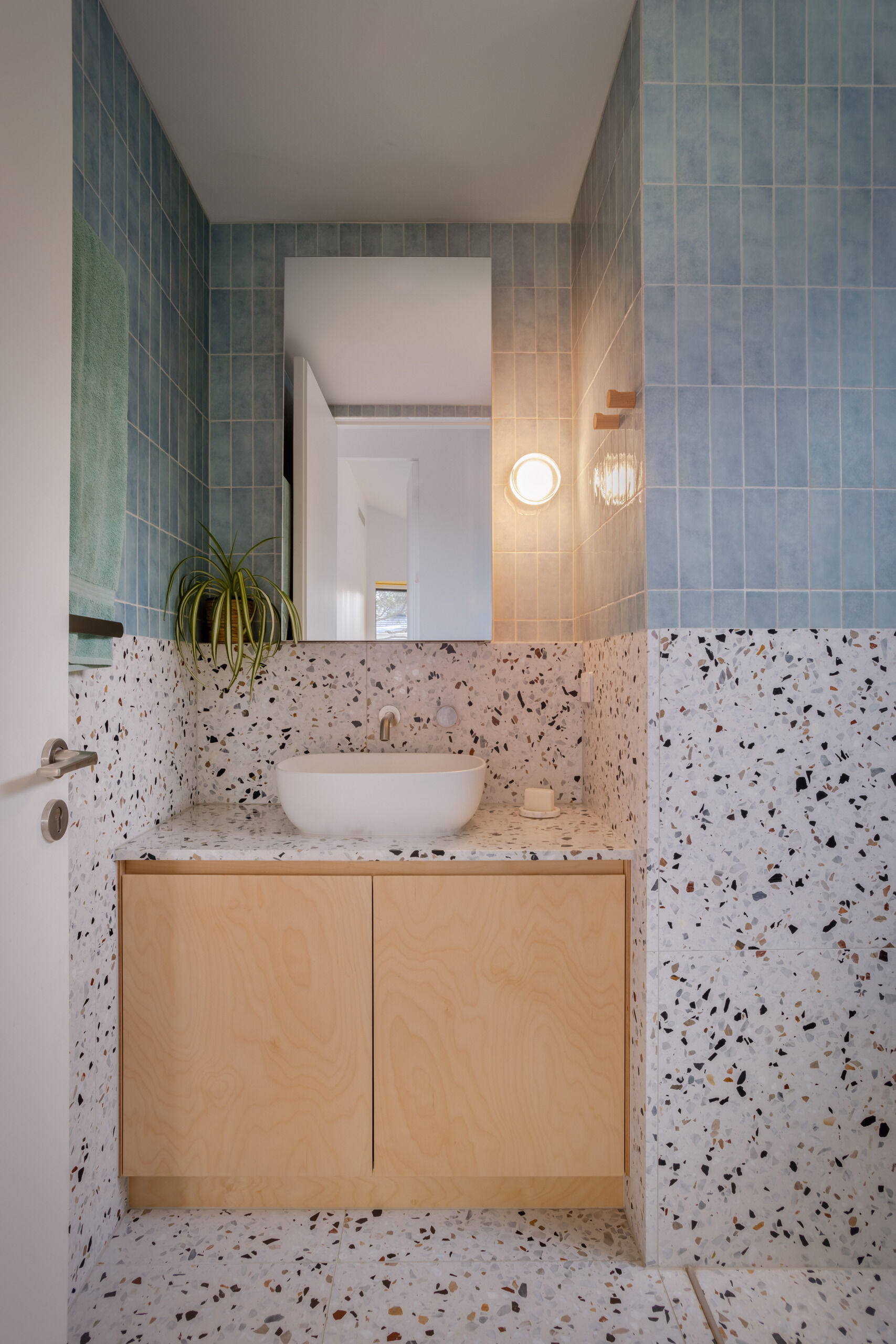 Shared by the younger family members, the kids' bathroom also features terrazzo tiles and vertical blue subway tiles, while wood accents and plants add a natural touch. 