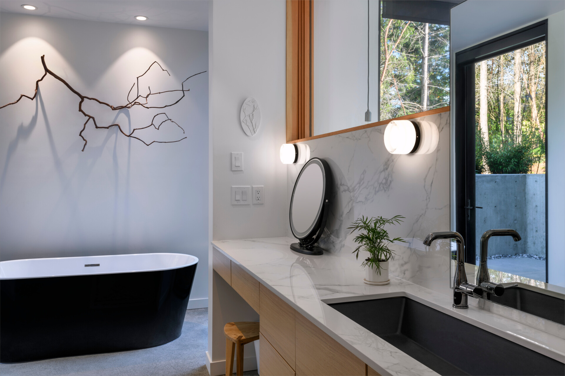 This modern bathroom blends clean lines with natural textures, featuring a floating wood vanity, soaking tub, and views into the surrounding trees.
