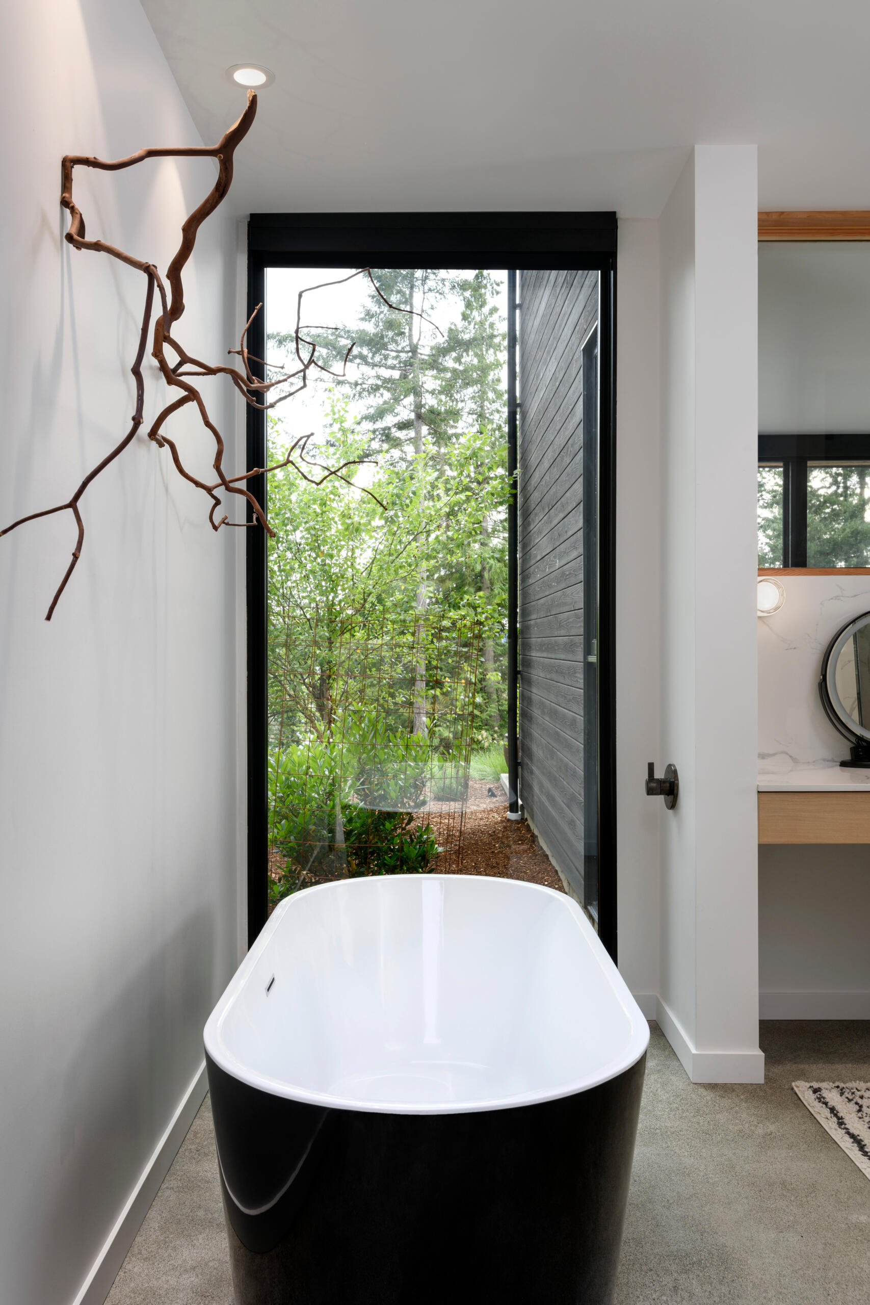 This modern bathroom blends clean lines with natural textures, featuring a floating wood vanity, soaking tub, and views into the surrounding trees.