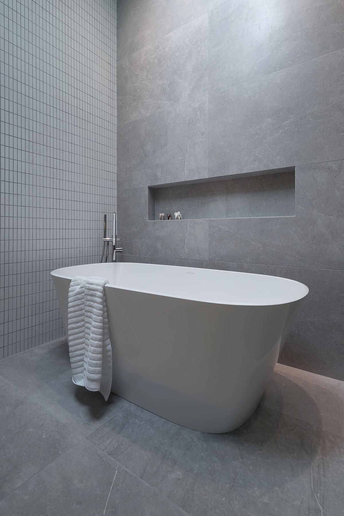 A modern marble and tile bathroom with a freestanding bathtub and shelving niche.