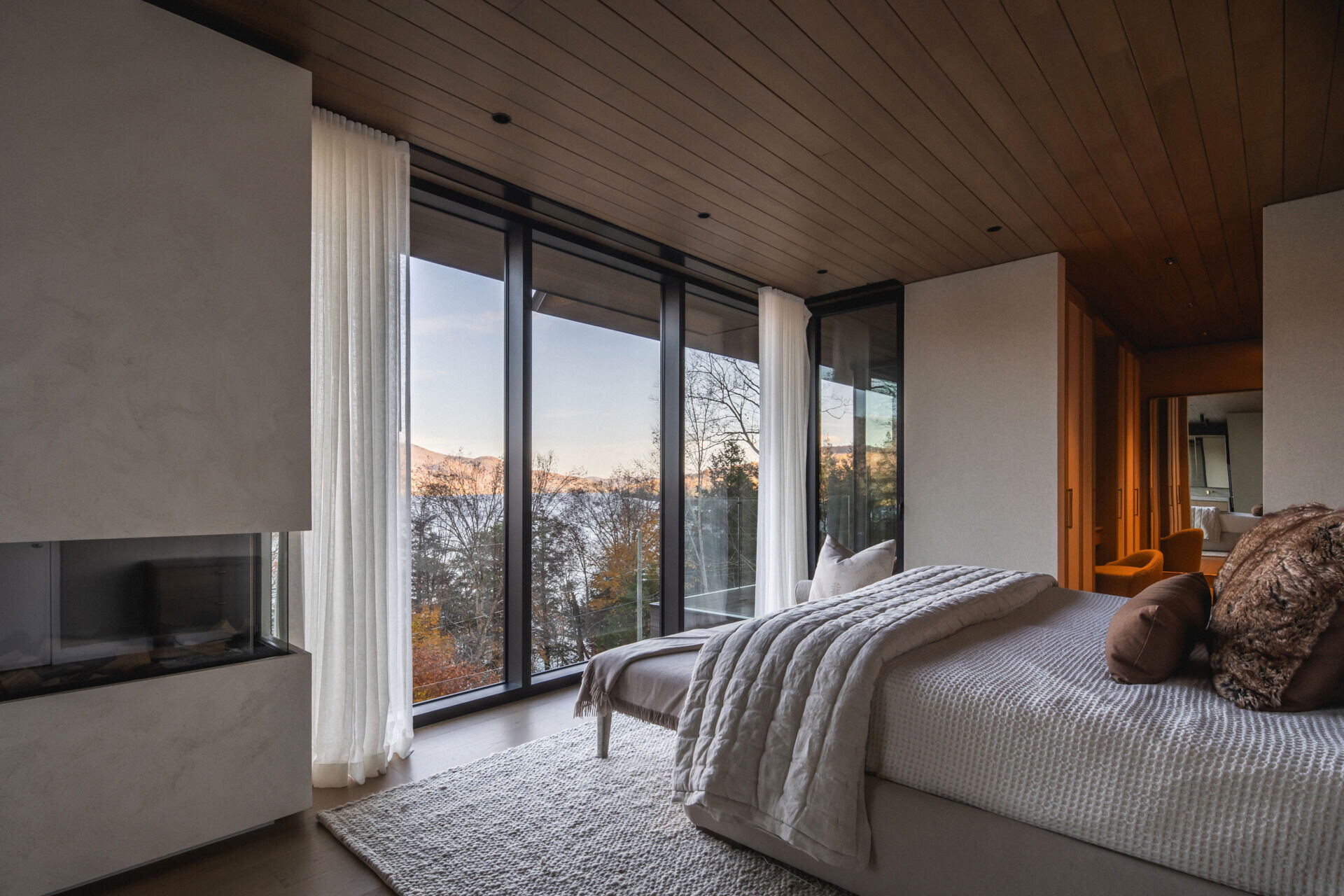 The primary suite includes a fireplace, floor-to-ceiling windows, and sweeping lake views. There's also a walk-in closet finished with wood doors offering generous storage.
