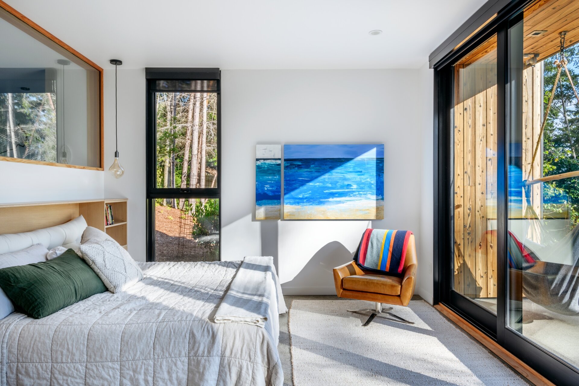 Crisp white walls, a textured rug, and a vintage leather chair create a relaxed, lived-in feel in this light-filled bedroom retreat.