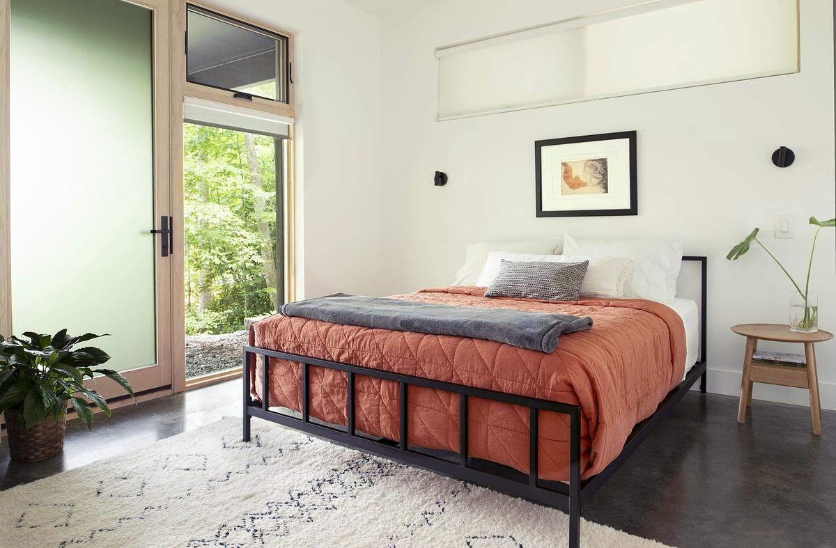 The guest bedroom is located under the cantilevered private volume and opens onto a lower deck. This setup provides guests with their own cozy outdoor space and a unique feeling of being nestled among the trees.