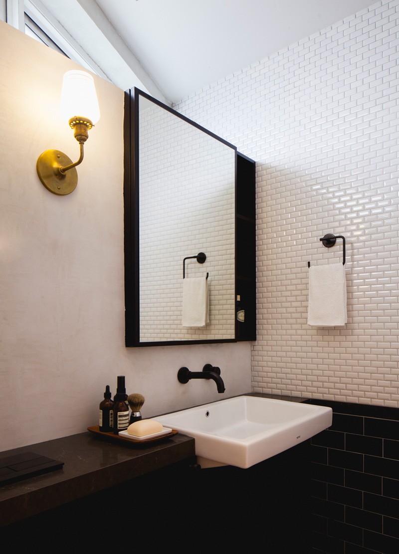 Behind a black accent wall in a bedroom, a walk-in closet leads to a sleek bathroom with white penny tiles and black fixtures.