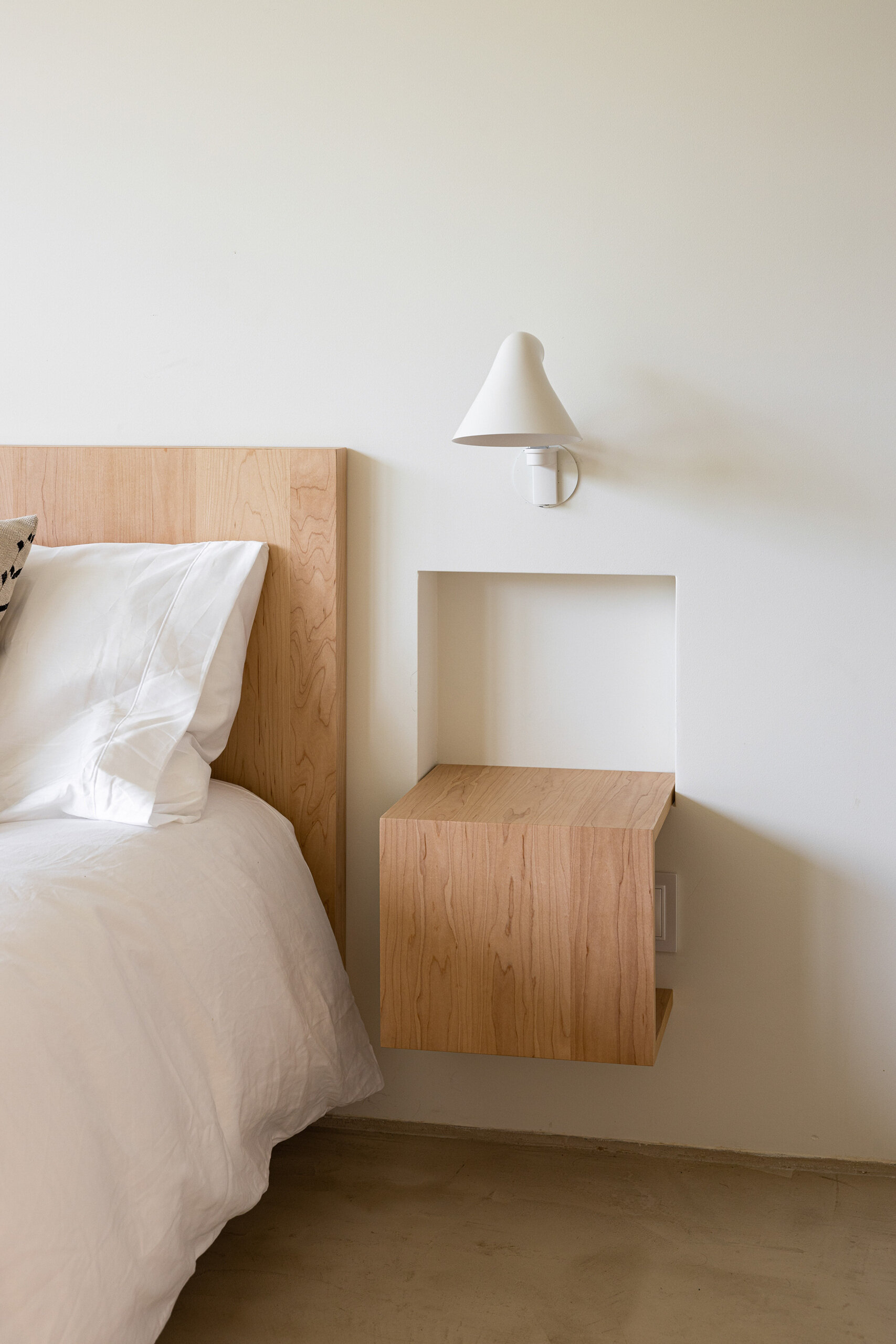 The bedroom is a continuation of calm with wood accents like built-in bedside tables, open shelving, and a desk, while large windows draw nature in.