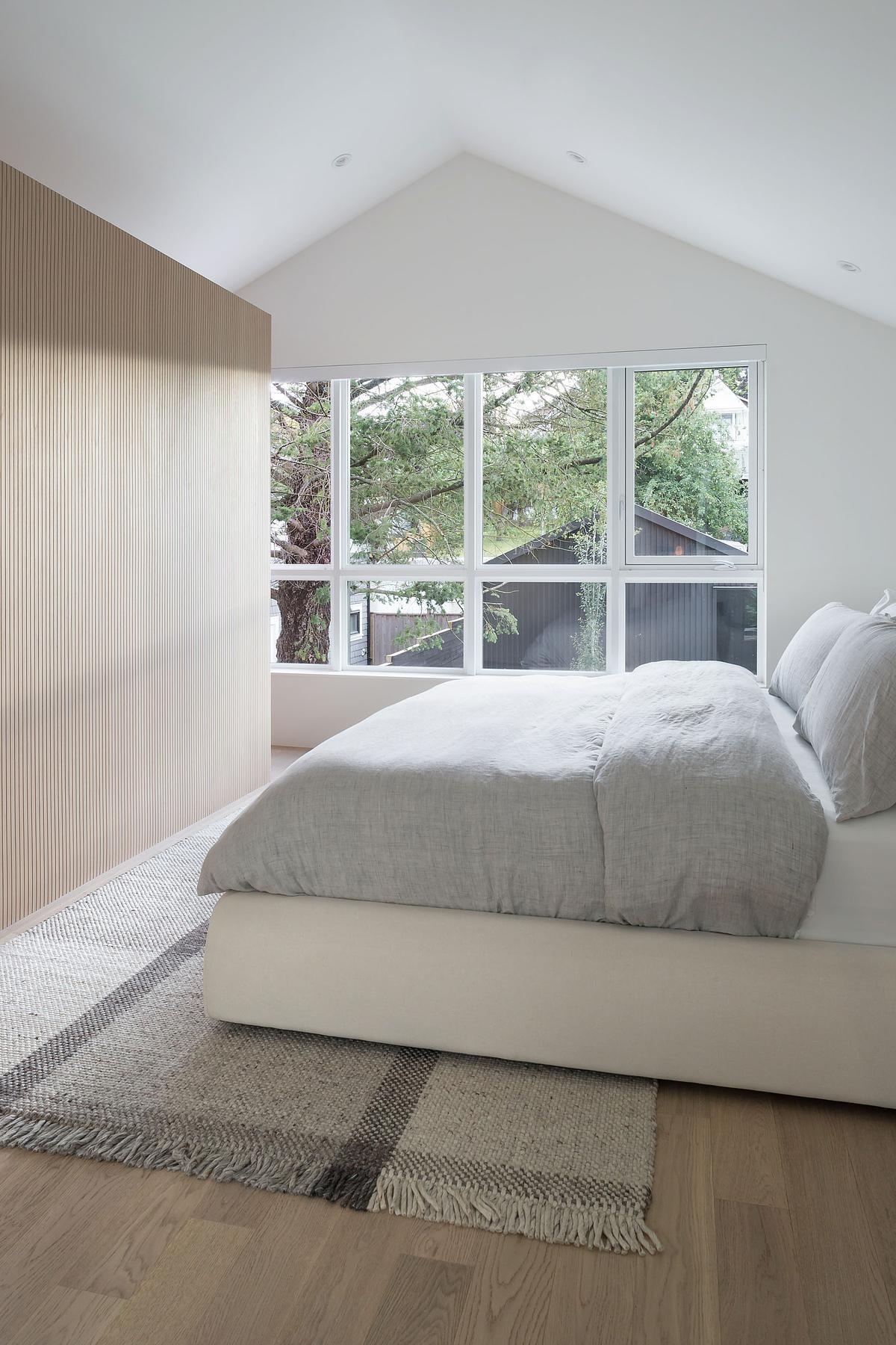 Minimal white walls and a warm wood partition define this peaceful bedroom retreat, quiet, considered, and beautifully restrained.