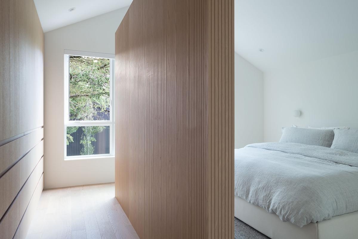 Minimal white walls and a warm wood partition define this peaceful bedroom retreat, quiet, considered, and beautifully restrained.