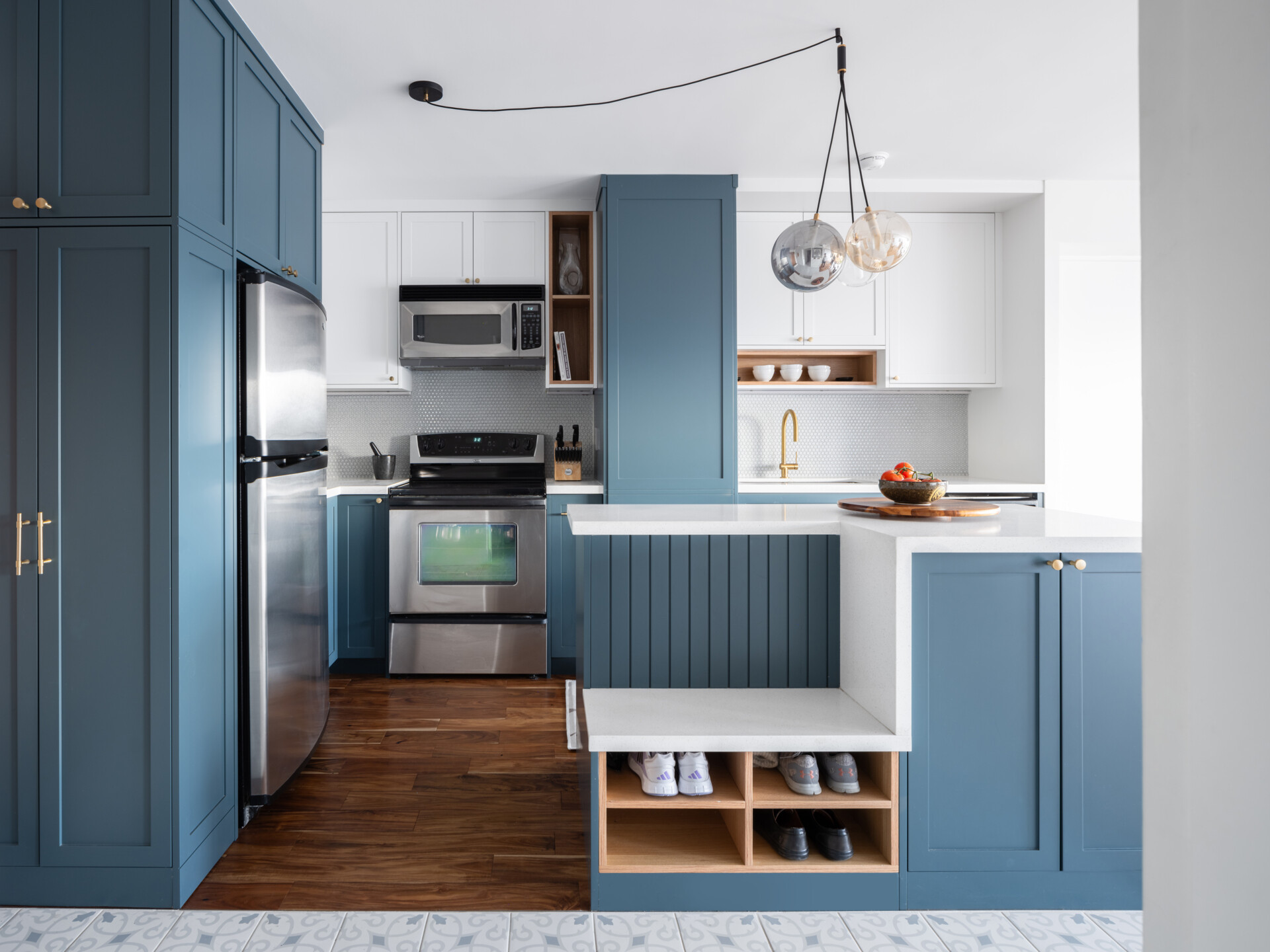 A reoriented kitchen with a blue and white color palette, has a dual-purpose island bringing storage, seating, and flow to the heart of this apartment.
