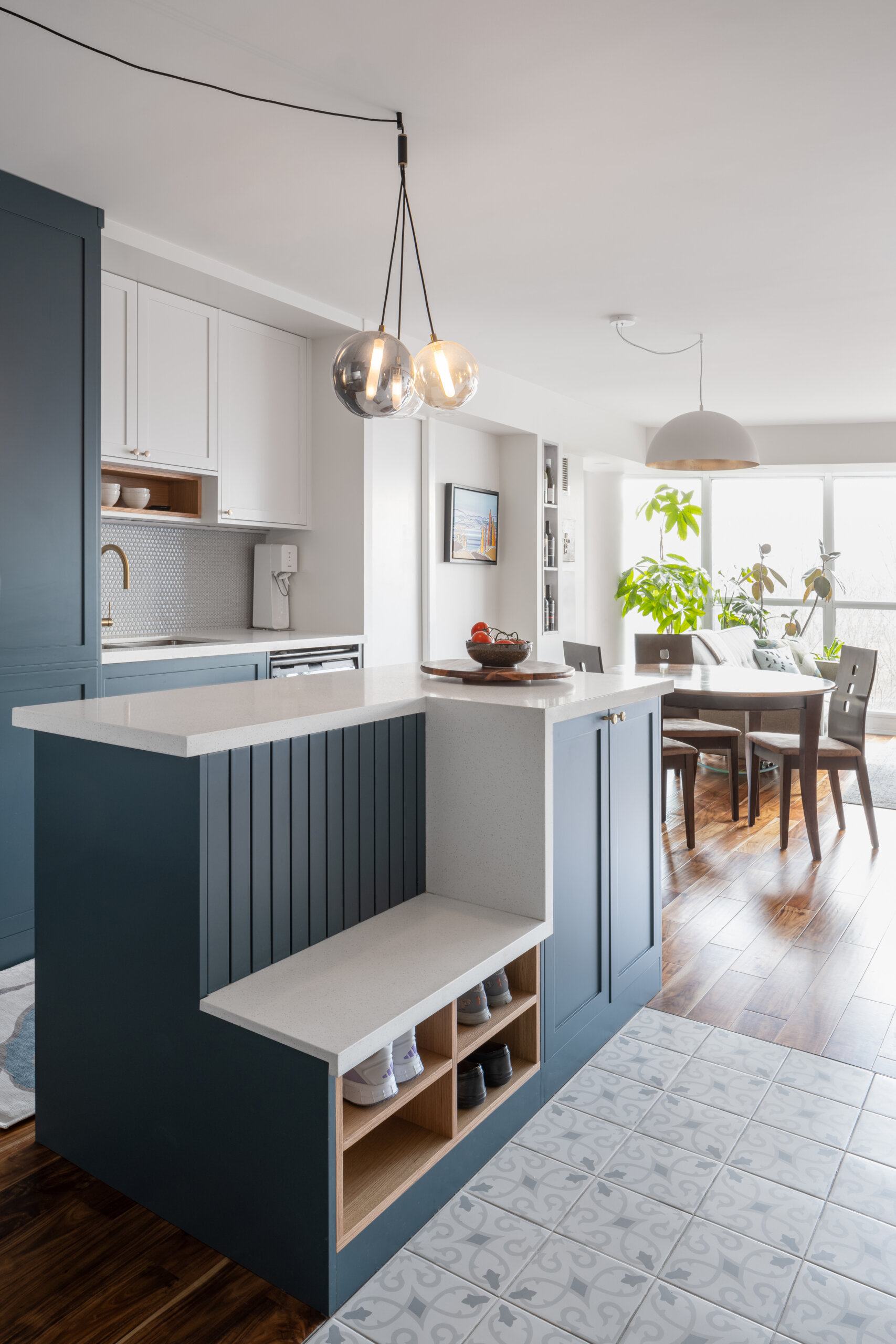 A reoriented kitchen with a blue and white color palette, has a dual-purpose island bringing storage, seating, and flow to the heart of this apartment.