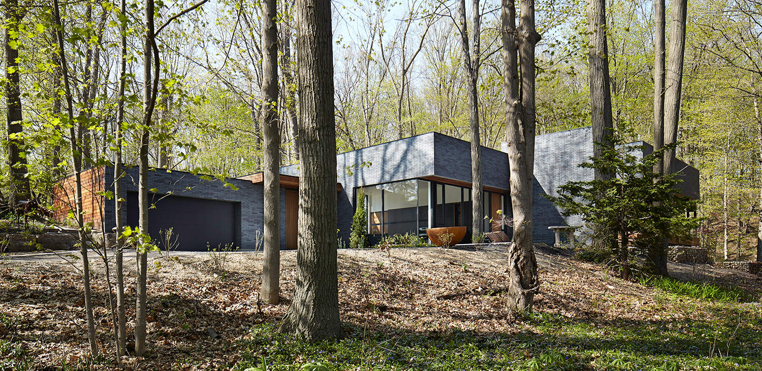 The home’s low, elongated form and earthy materials, like brick and wood, echo the tones of the escarpment and surrounding forest.