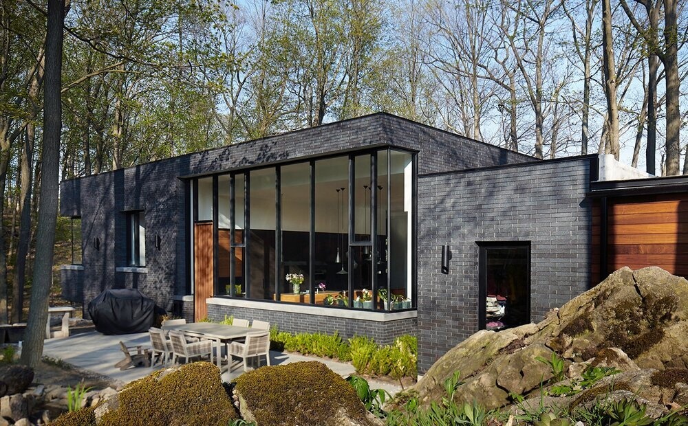 The home’s low, elongated form and earthy materials, like brick and wood, echo the tones of the escarpment and surrounding forest.
