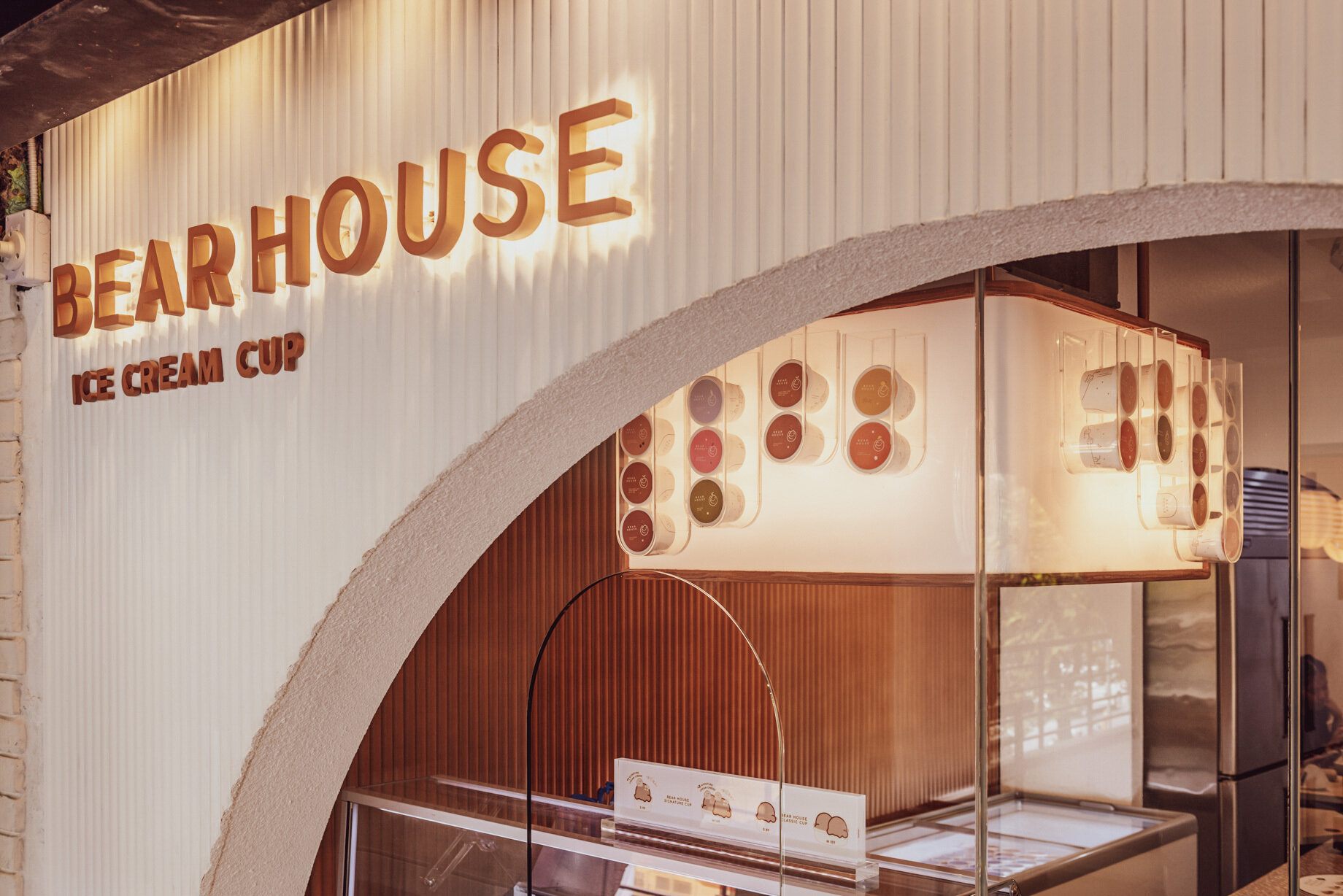 BEARHOUSE blends bubble tea and ice cream in a cozy café inspired by a bear cave and swirling ice cream textures. This small space uses soft two-tone colors and inviting built-in seating to create the perfect hangout.