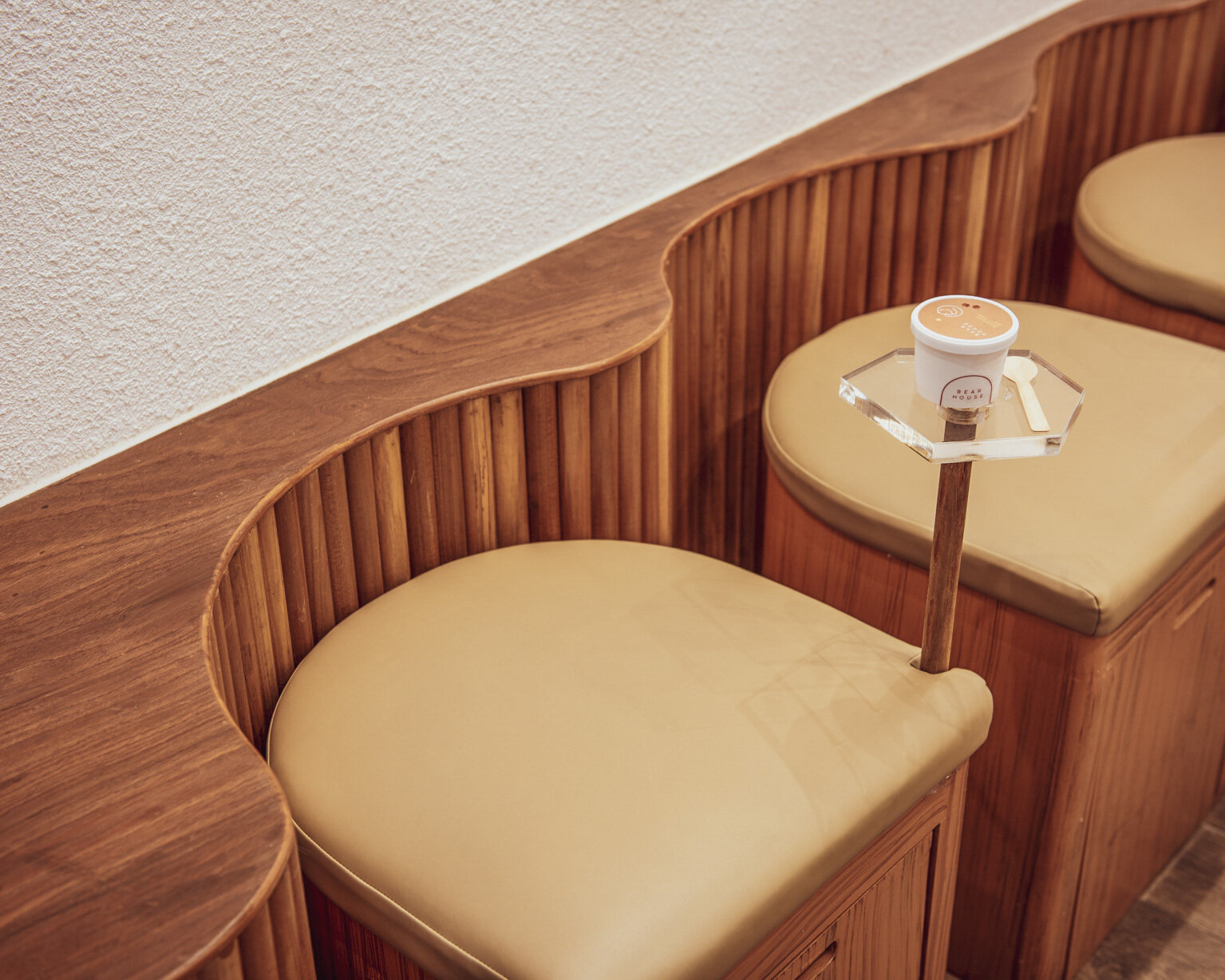 BEARHOUSE blends bubble tea and ice cream in a cozy café inspired by a bear cave and swirling ice cream textures. This small space uses soft two-tone colors and inviting built-in seating to create the perfect hangout.