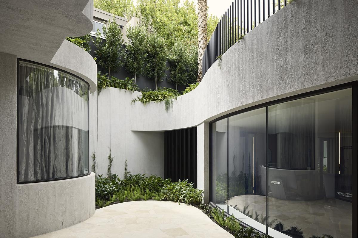 Natural rock cladding, curved forms, and expansive glazing define the sculptural exterior of this serene, modern Melbourne home.