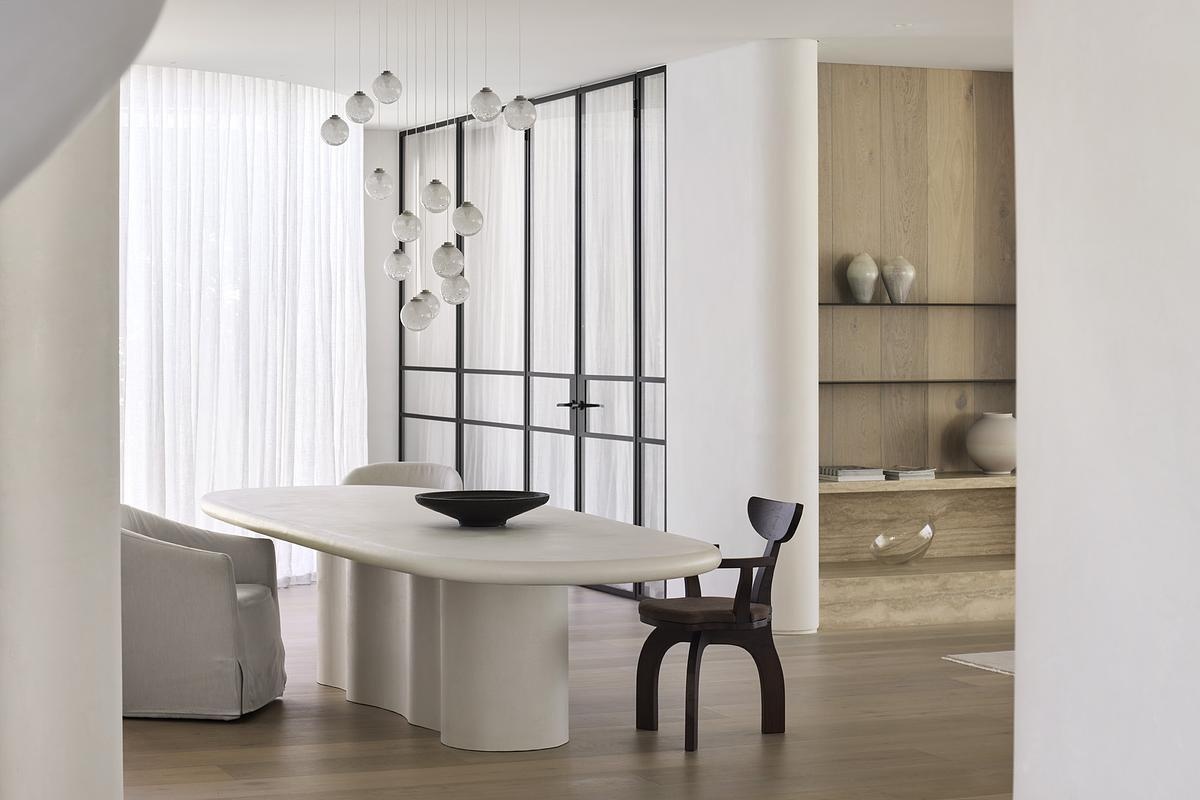 This calm, sculptural dining space features curved walls, sheer curtains, and soft lighting for a refined yet grounded atmosphere.