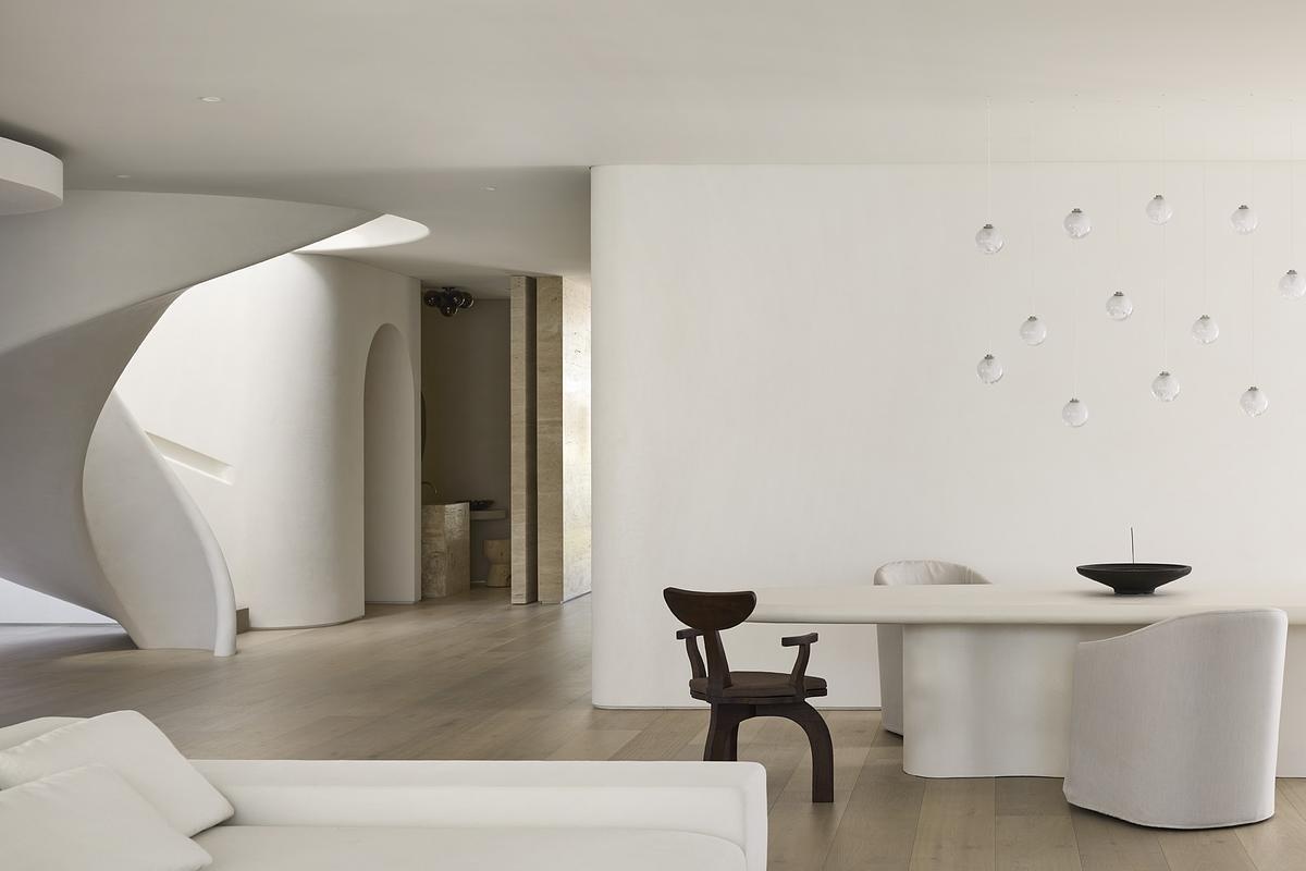 This calm, sculptural dining space features curved walls, sheer curtains, and soft lighting for a refined yet grounded atmosphere.