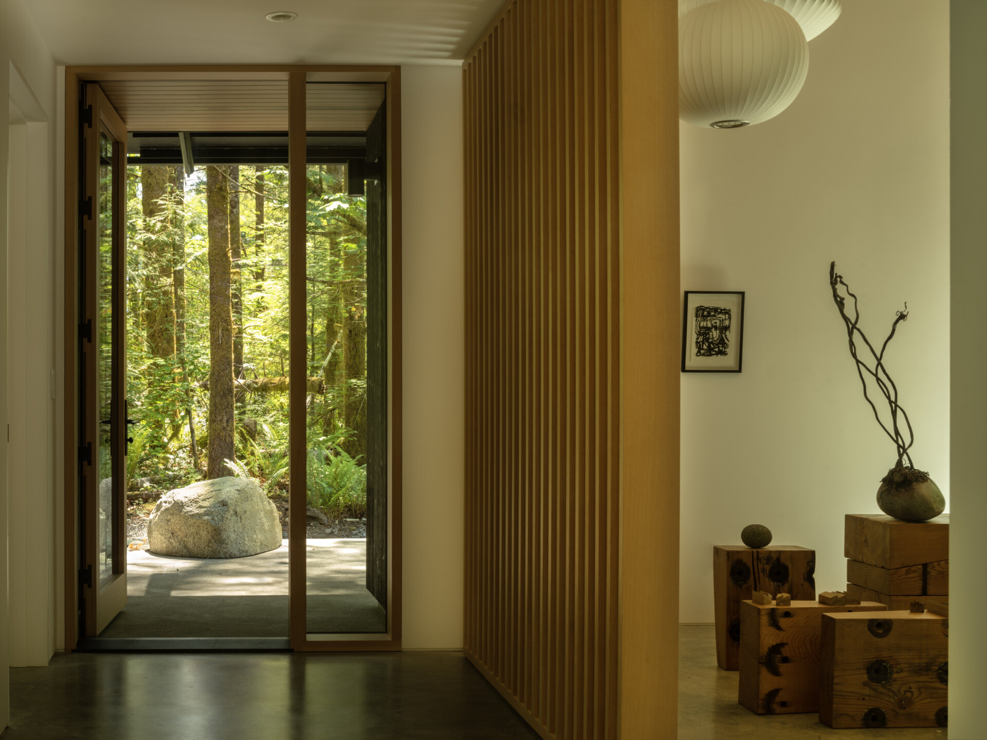 The entry blends natural textures with quiet modernity. A slatted wood screen adds privacy and rhythm, while stone and raw wood accents ground the space.