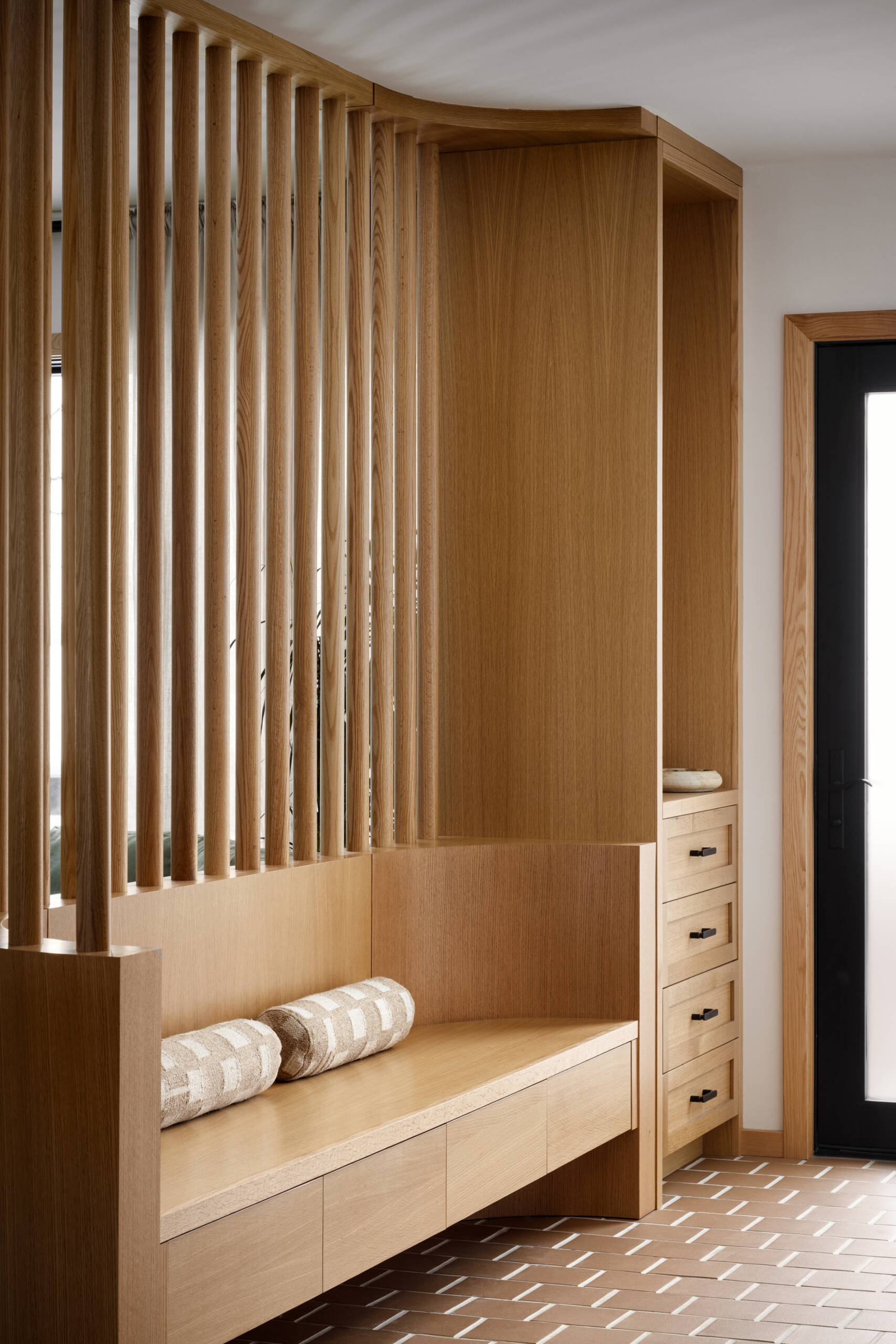 The entryway sets the tone for the entire home: calm, practical, and welcoming. A built-in bench with vertical wooden slats softens the squareness of the original floor plan, offering both seating and subtle separation from the main living area. Paired with warm wood and tile flooring, the design keeps the space light, grounded, and organized, ideal for a busy family coming and going.