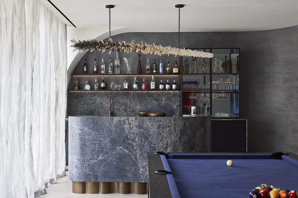 The entertainment zone of a modern home includes a DJ booth and opens onto a private courtyard, balancing boldness and ease. A cocktail bar accented with bronze and brass speaks to the home's quiet sense of glamour.