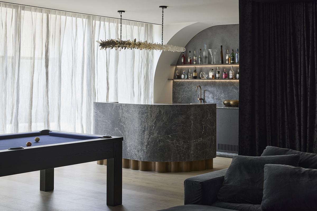 The entertainment zone of a modern home includes a DJ booth and opens onto a private courtyard, balancing boldness and ease. A cocktail bar accented with bronze and brass speaks to the home's quiet sense of glamour.