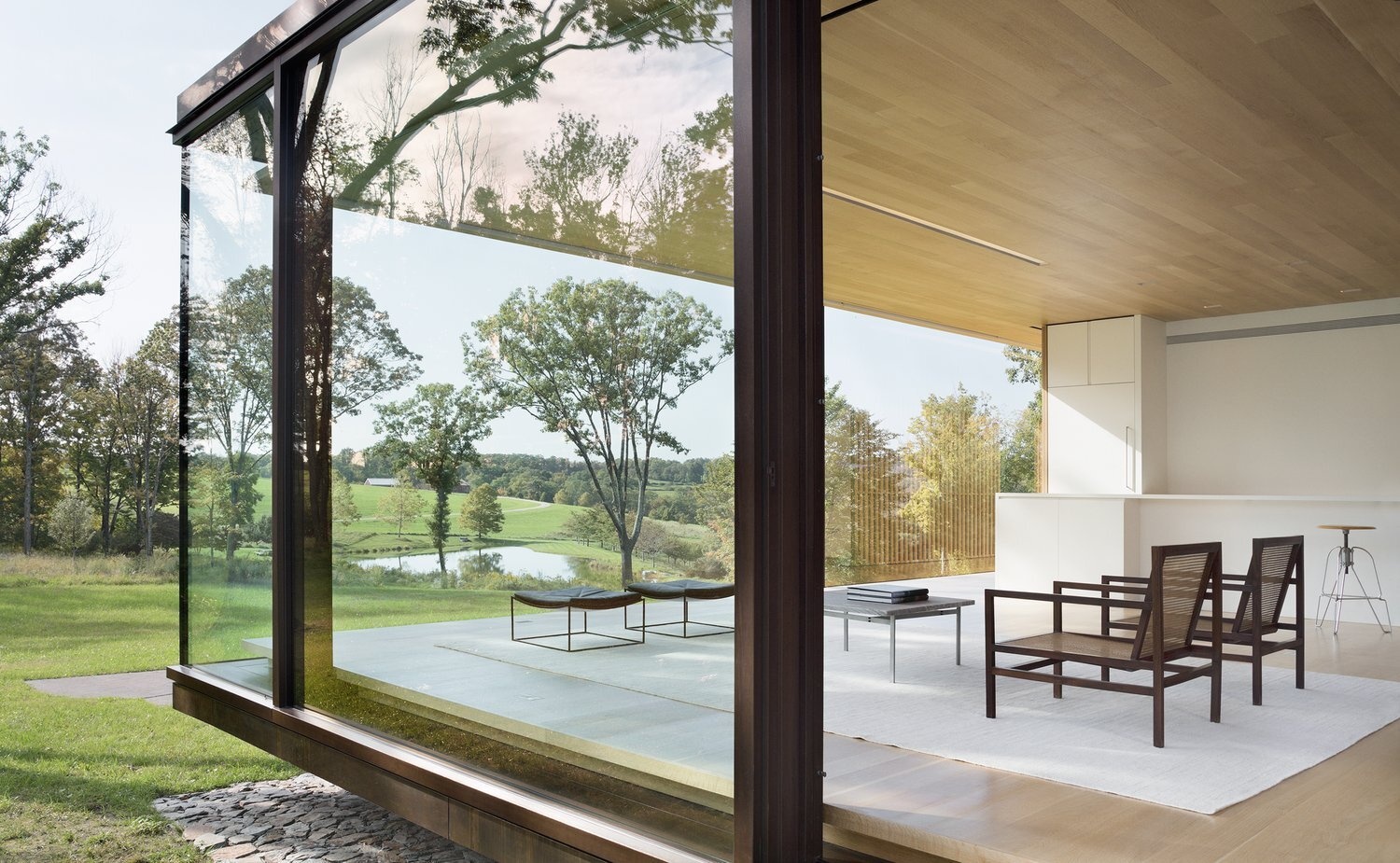Framed by floor-to-ceiling glass, the living area feels immersed in nature, with light filtering through the glowing wood core by night.