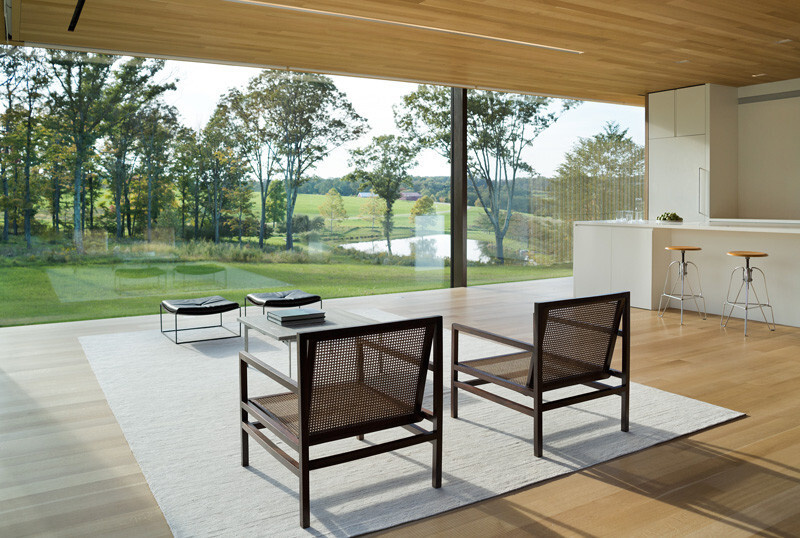 Framed by floor-to-ceiling glass, the living area feels immersed in nature, with light filtering through the glowing wood core by night.