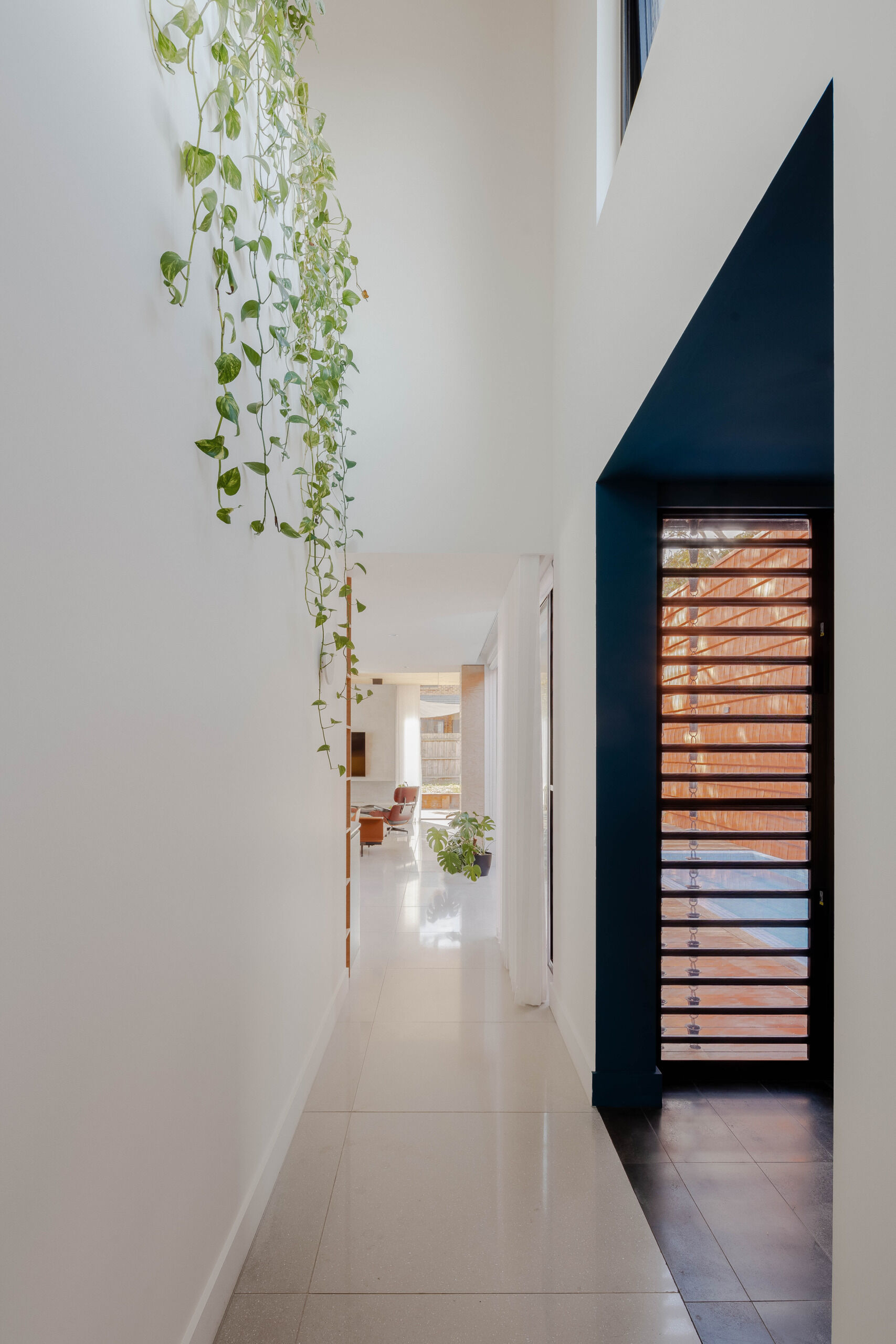 The hallway acts as a circulation spine, connecting the two living pods. Its role is more than functional. It visually frames the home’s interior plant life and allows shifting glimpses of the trees outside. It’s a passage shaped by nature, not just design.