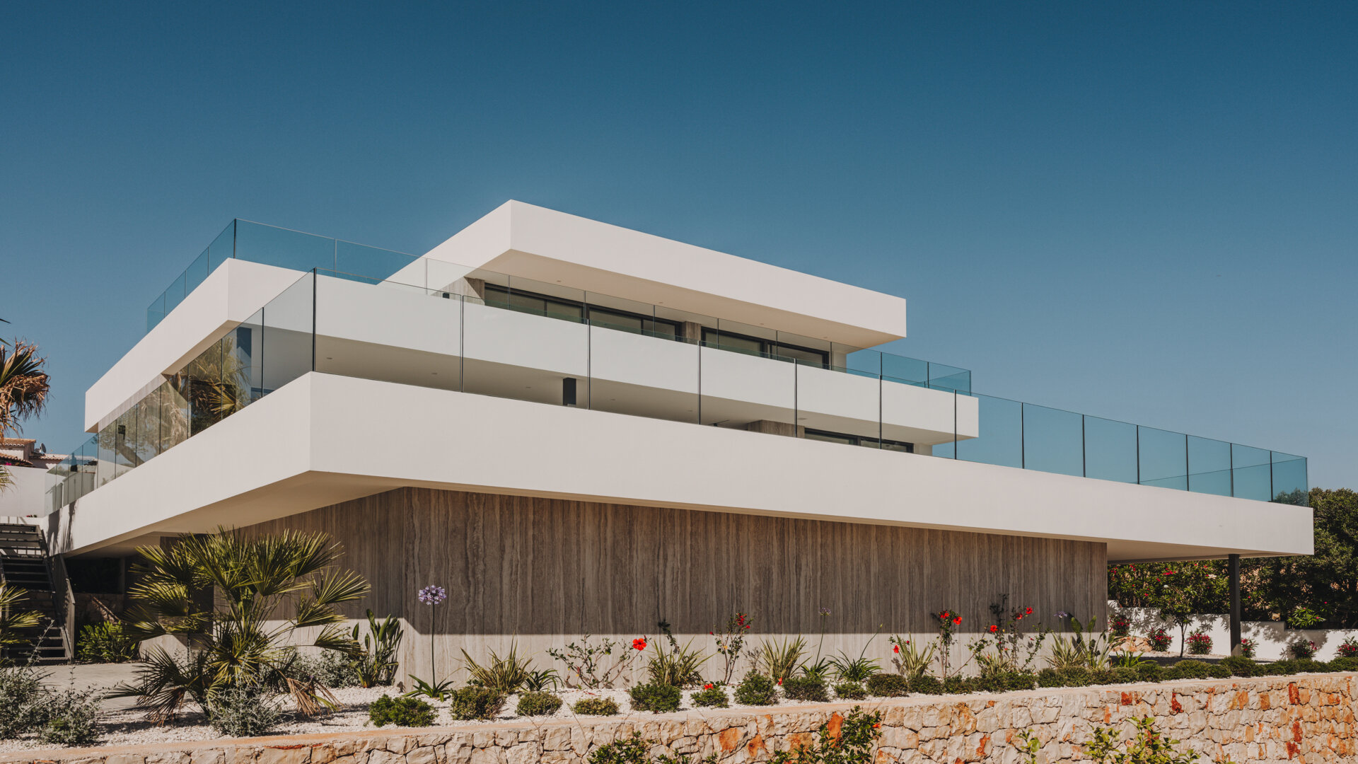 Travertine walls and oak accents define this layered coastal home that blends seamlessly into the slope.
