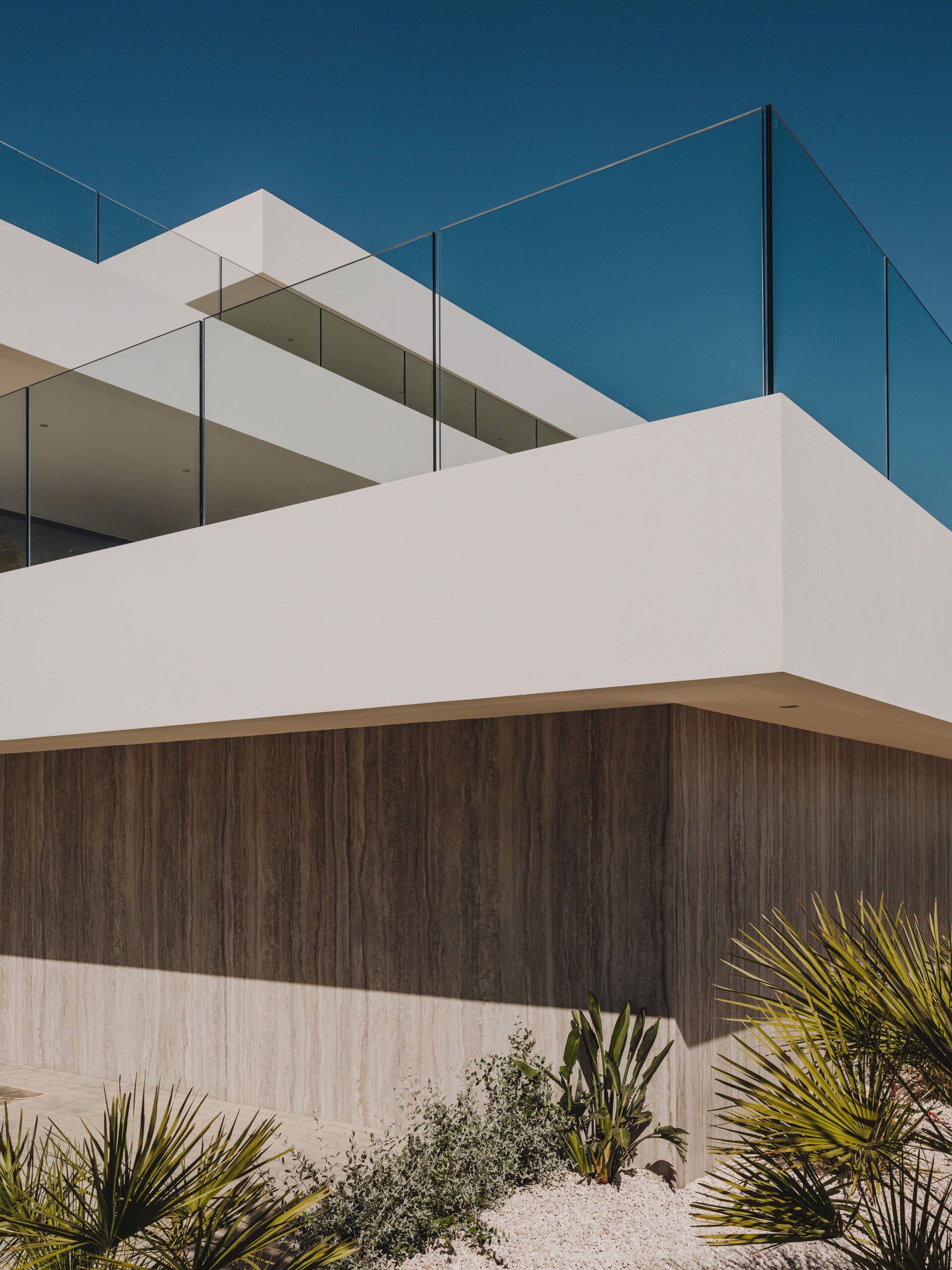Travertine walls and oak accents define this layered coastal home that blends seamlessly into the slope.