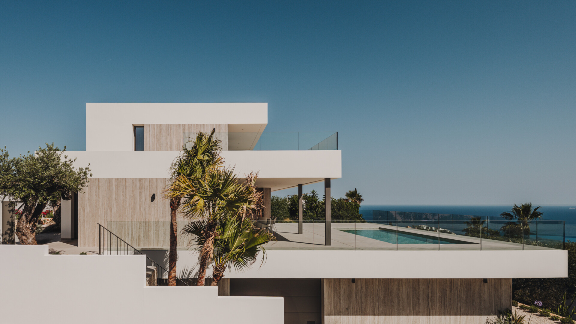 Travertine walls and oak accents define this layered coastal home that blends seamlessly into the slope.