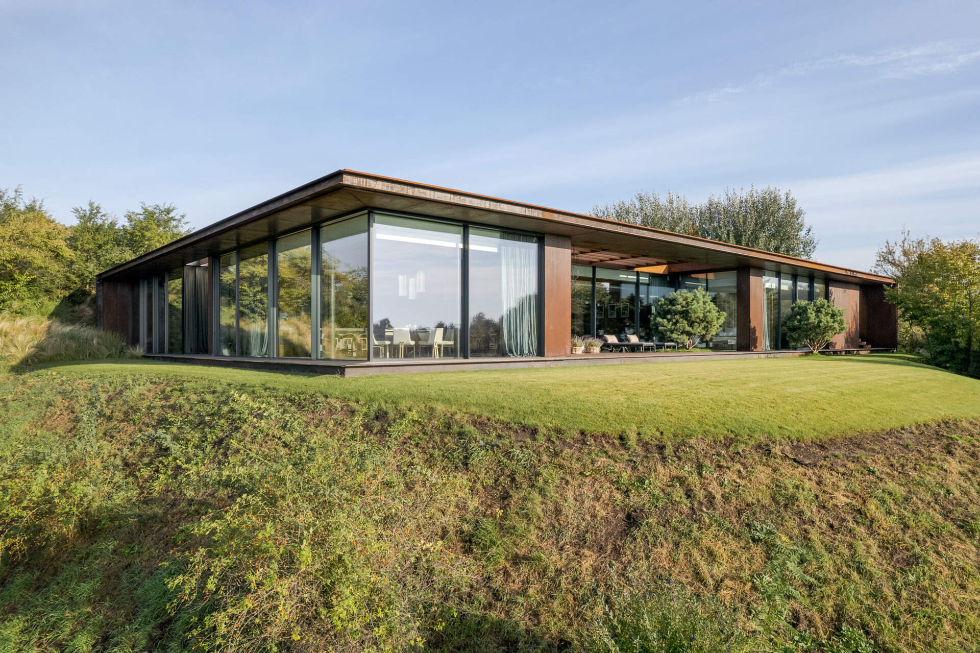 This modern home vanishes into the hillside with a green roof, corten steel facade, and panoramic river views.