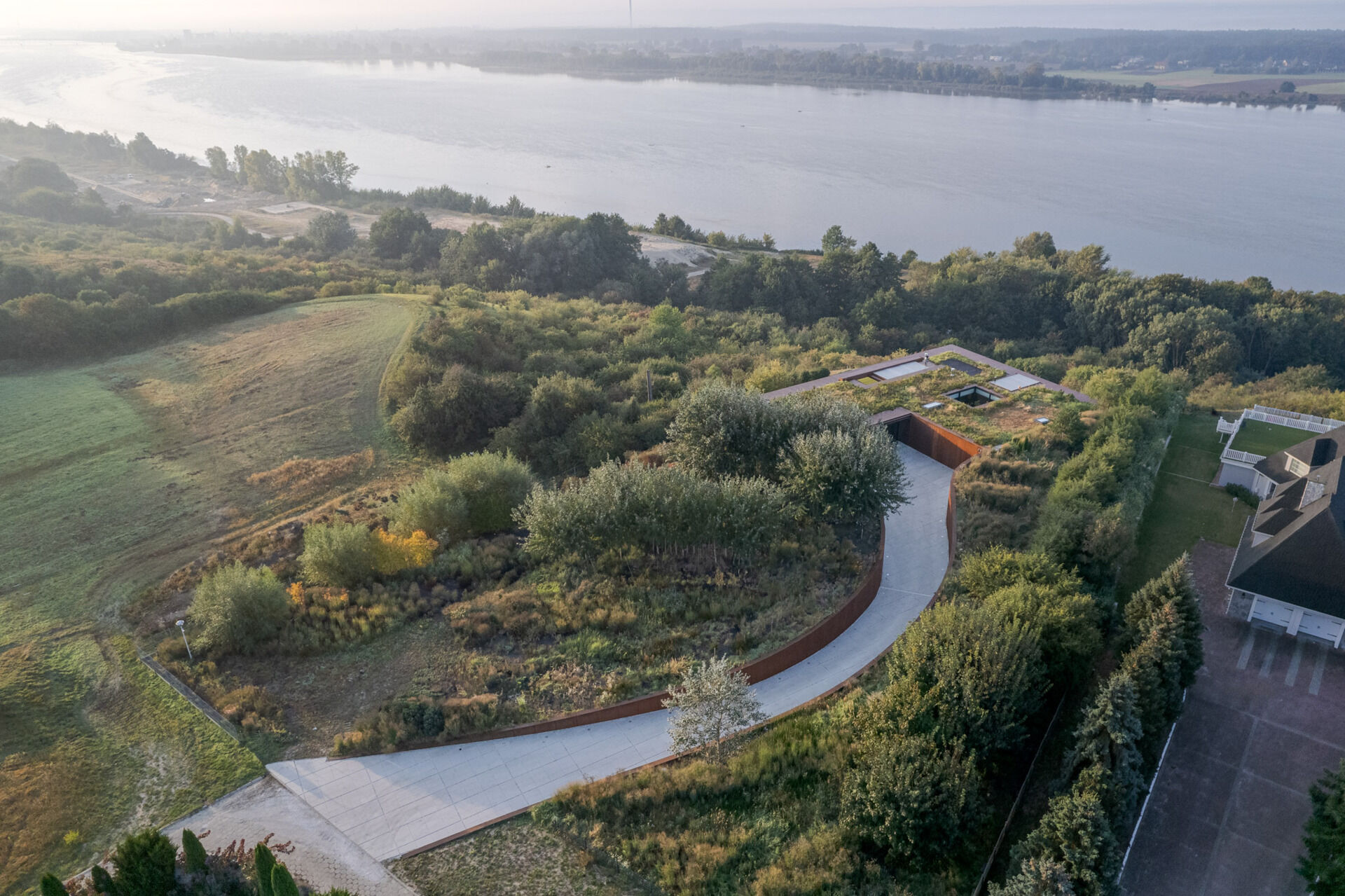 This modern home vanishes into the hillside with a green roof, corten steel facade, and panoramic river views.