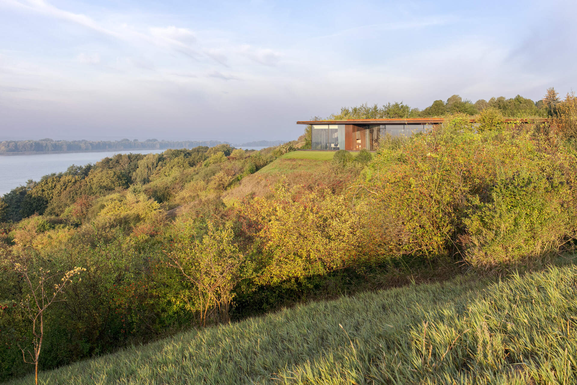This modern home vanishes into the hillside with a green roof, corten steel facade, and panoramic river views.