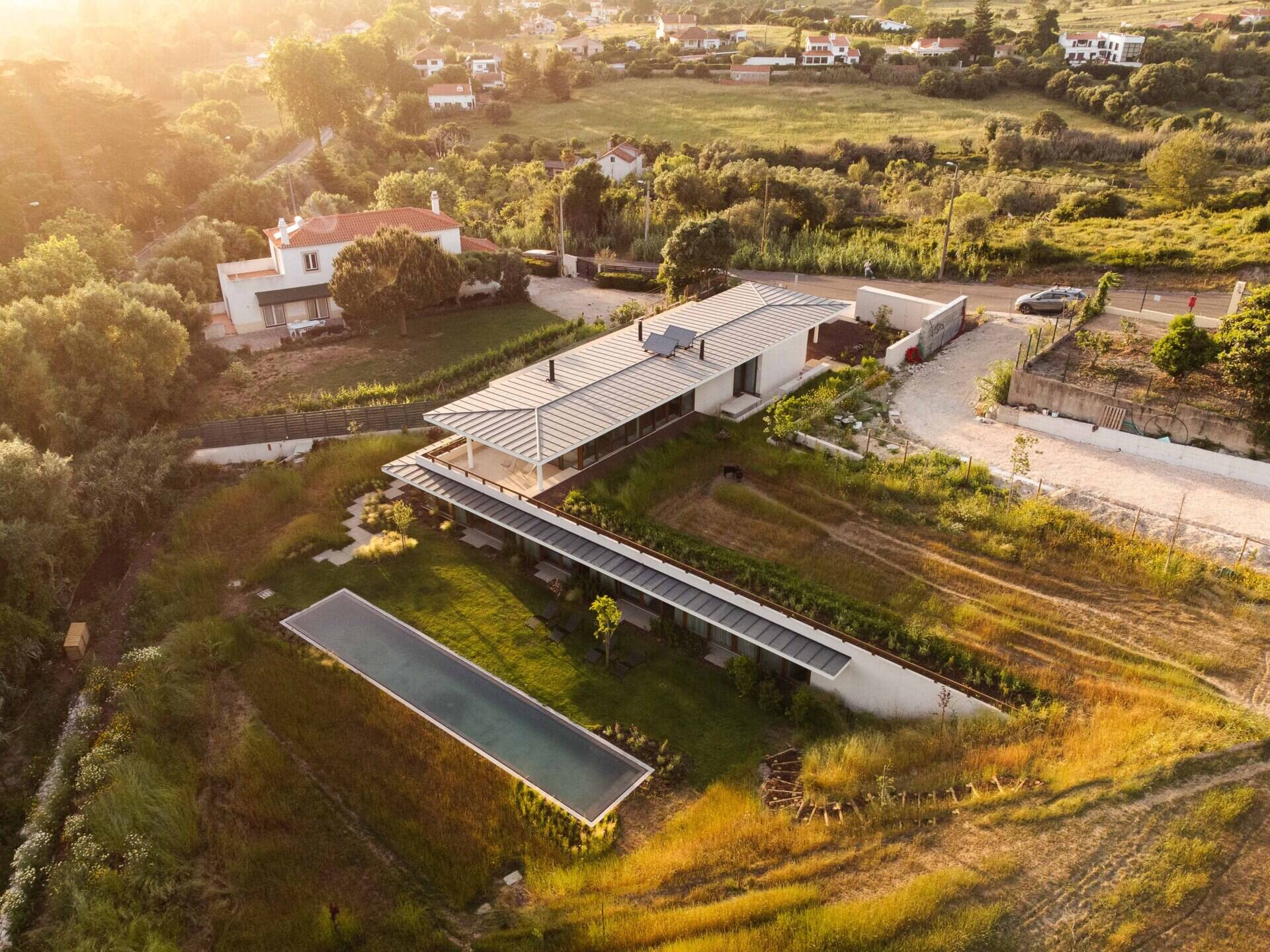 This hillside home uses the natural slope to its advantage. Half-buried and minimal in form, it blends seamlessly with its environment. The green roof disappears into the landscape, helping regulate temperature while softening the structure’s visual impact.