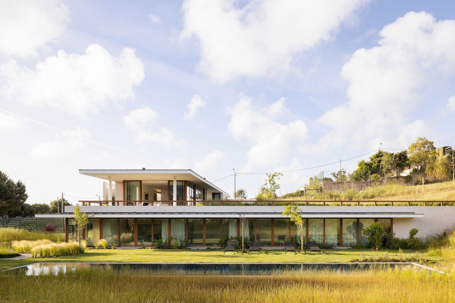 This hillside home uses the natural slope to its advantage. Half-buried and minimal in form, it blends seamlessly with its environment. The green roof disappears into the landscape, helping regulate temperature while softening the structure’s visual impact.