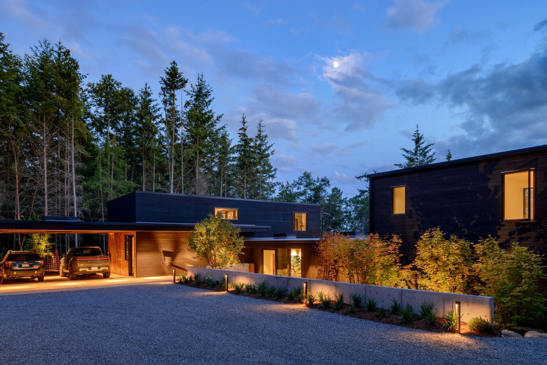 A stepped, low-profile home clad in charred yakisugi siding, designed to blend into the hillside and forest.
