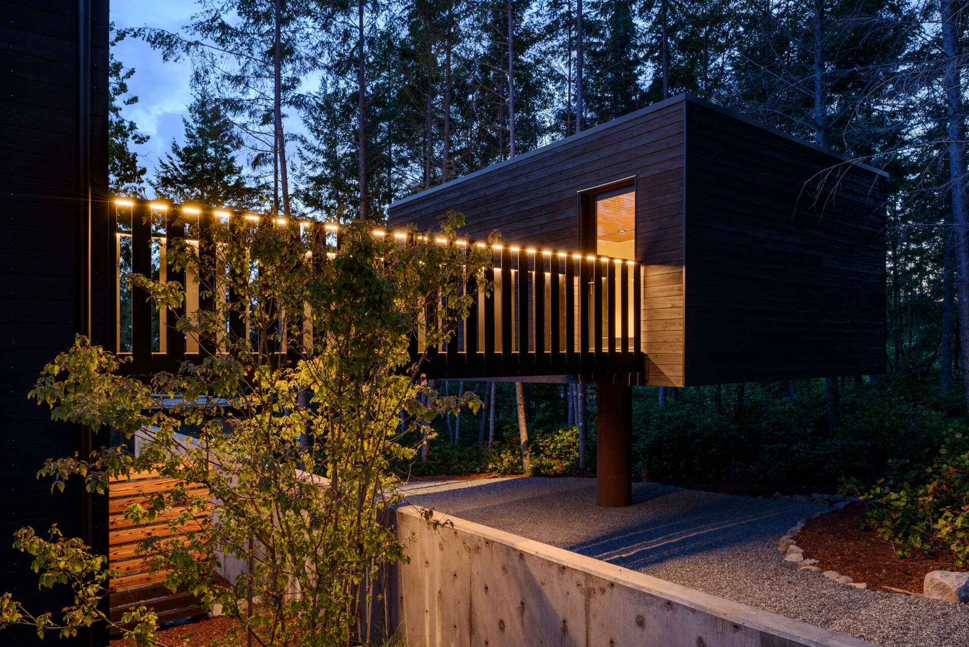 A stepped, low-profile home clad in charred yakisugi siding, designed to blend into the hillside and forest.