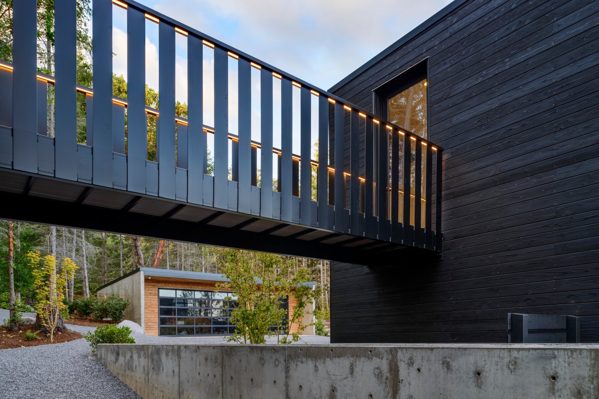 A stepped, low-profile home clad in charred yakisugi siding, designed to blend into the hillside and forest.