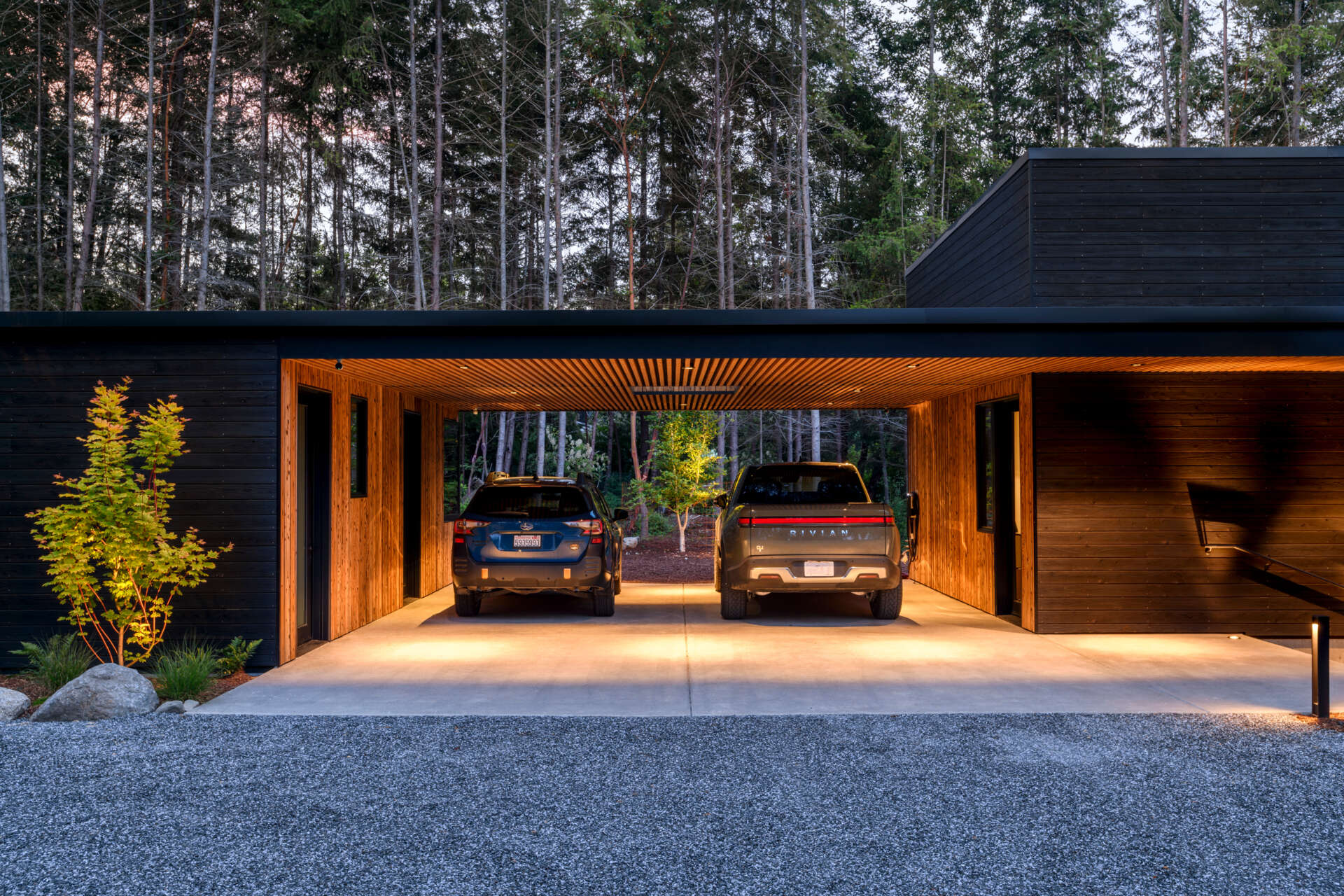 A stepped, low-profile home clad in charred yakisugi siding, designed to blend into the hillside and forest.