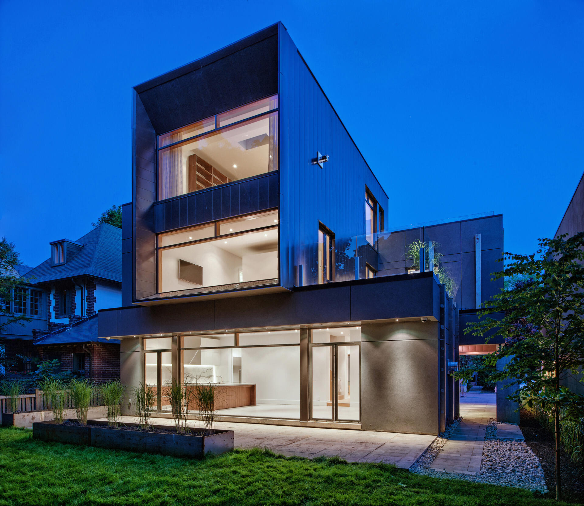 Expansive windows and a shaded rear yard connect this modern Toronto home to the ravine canopy behind it. Designed by Tact Design, the rear exterior offers a quiet, nature-focused escape.
