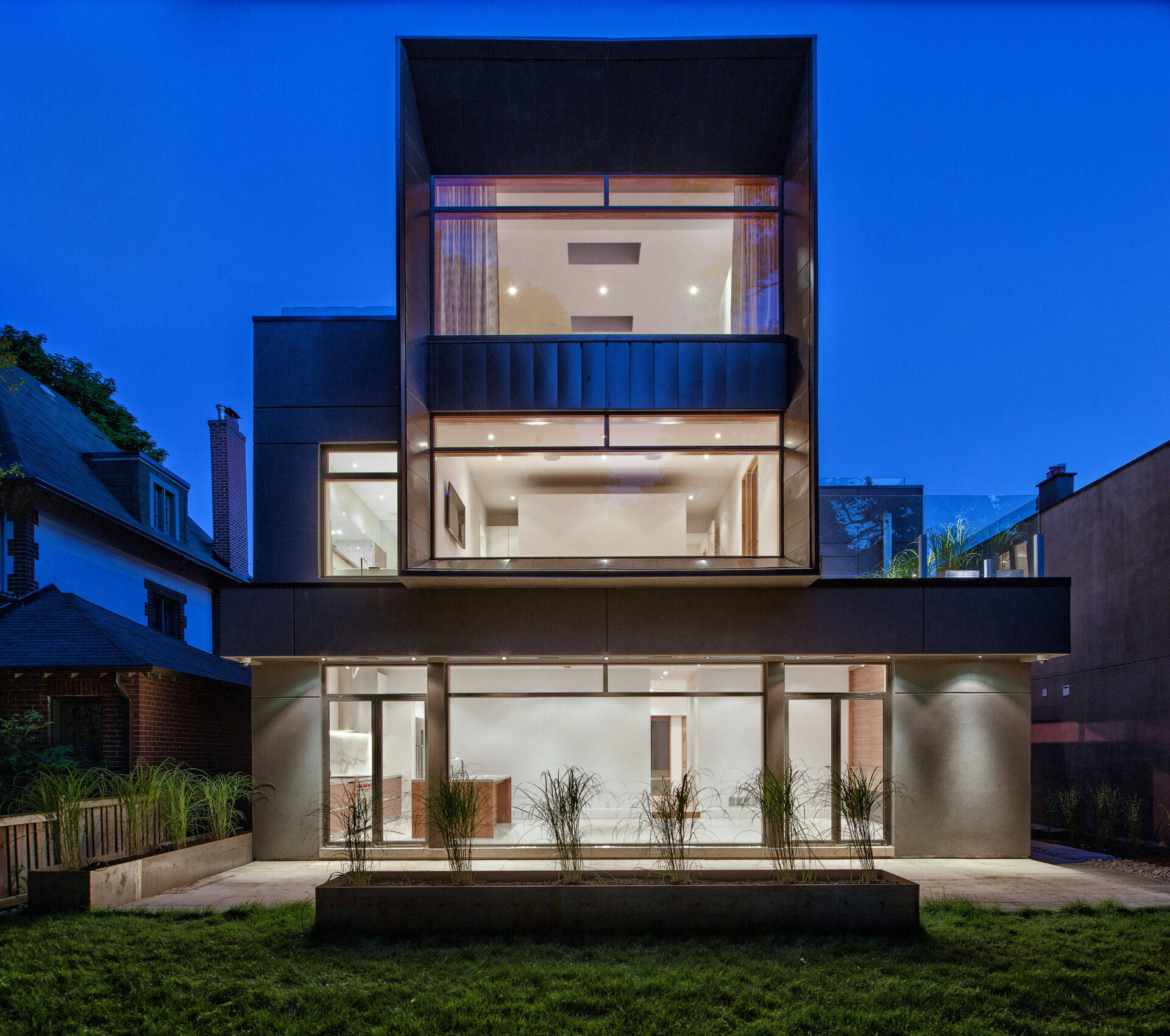 Expansive windows and a shaded rear yard connect this modern Toronto home to the ravine canopy behind it. Designed by Tact Design, the rear exterior offers a quiet, nature-focused escape.