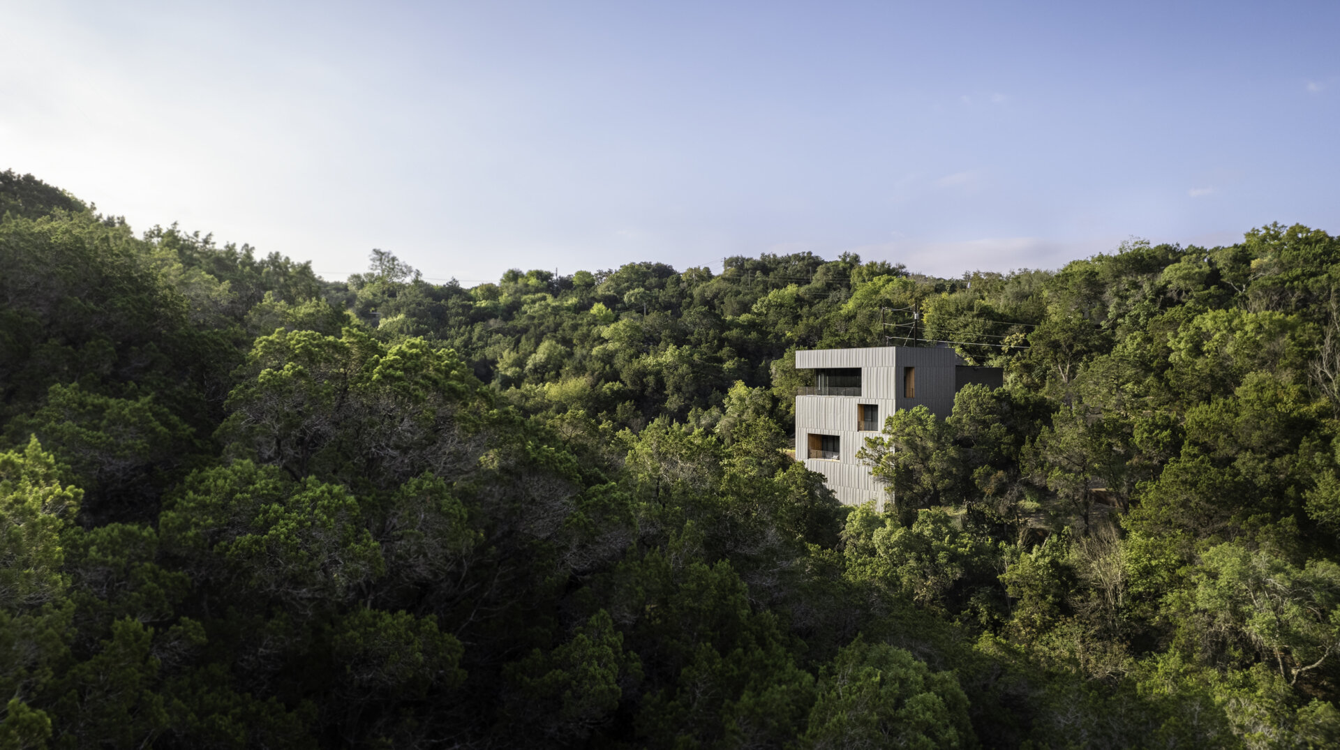 The exterior of this modern home is wrapped in vertical steel panels designed to weather, while deep wood-lined recesses frame curated views and allow light to shift throughout the day.