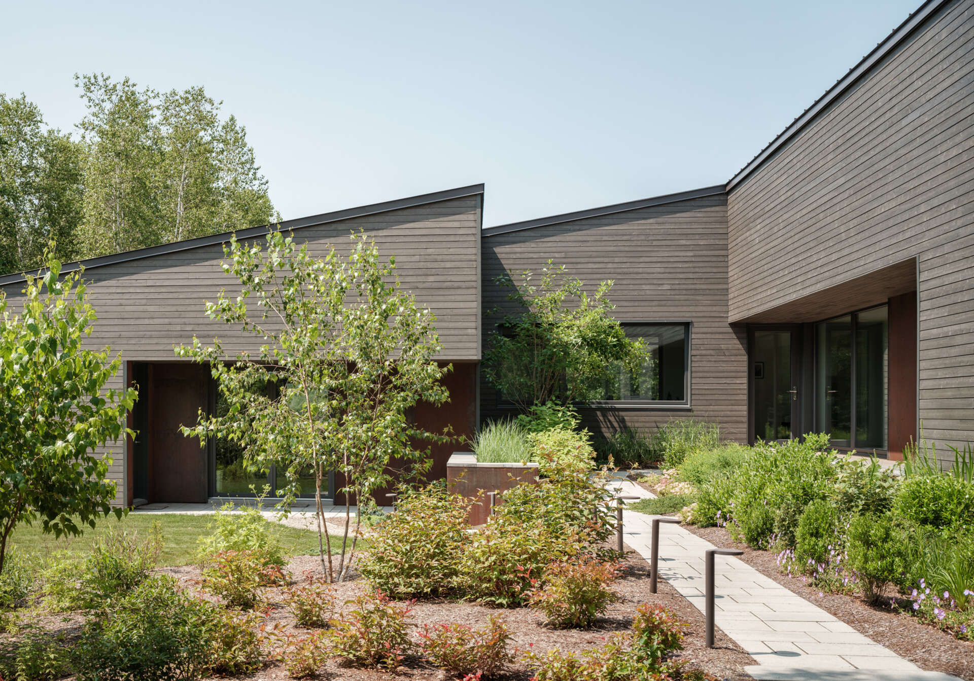 Stained cedar siding and Corten steel panels give this house a modern, grounded look that blends beautifully with the wooded riverside landscape.